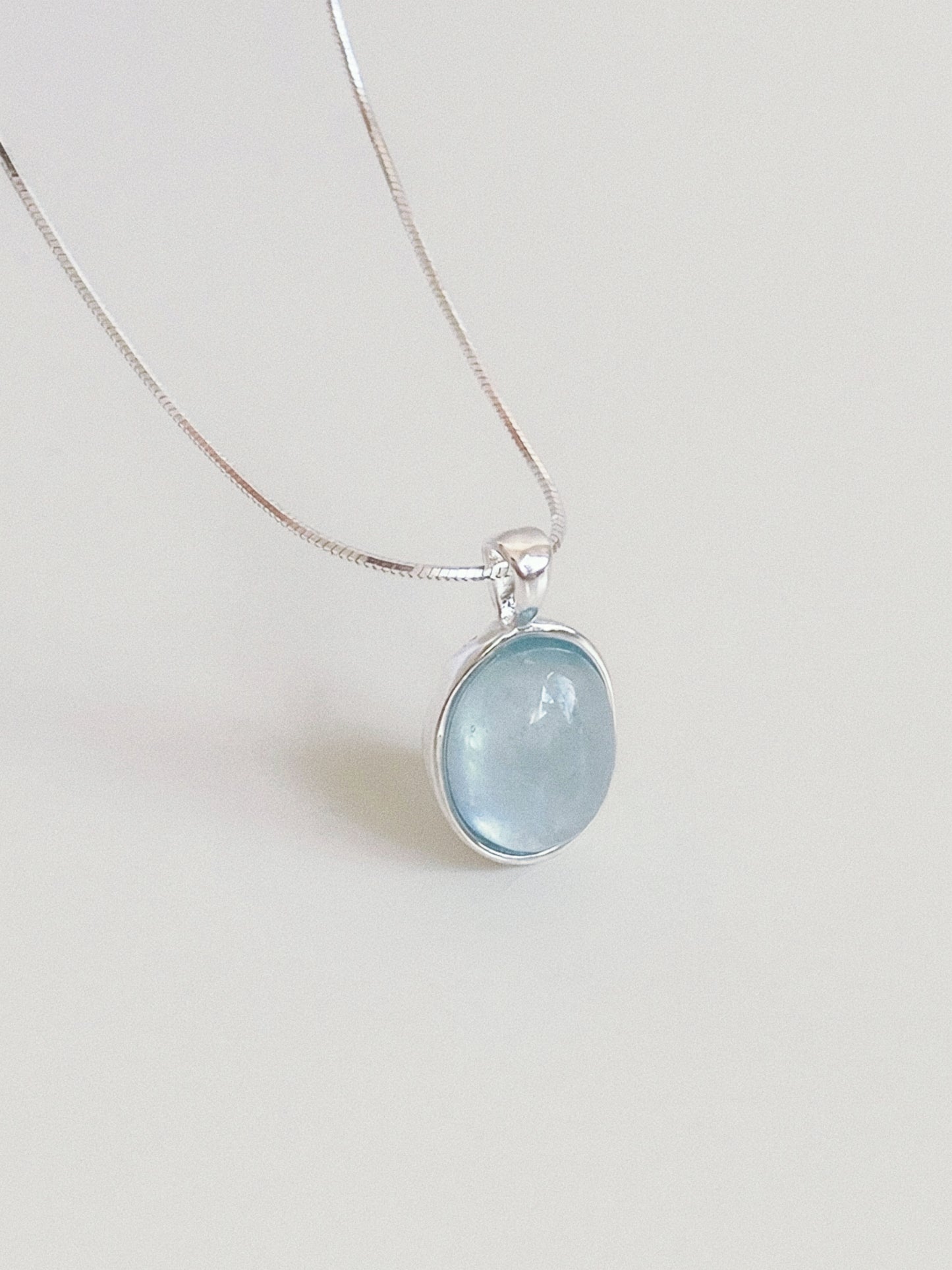 Natural aquamarine oval cabochon pendant in a textured sterling silver bezel hanging on a fine round snake chain