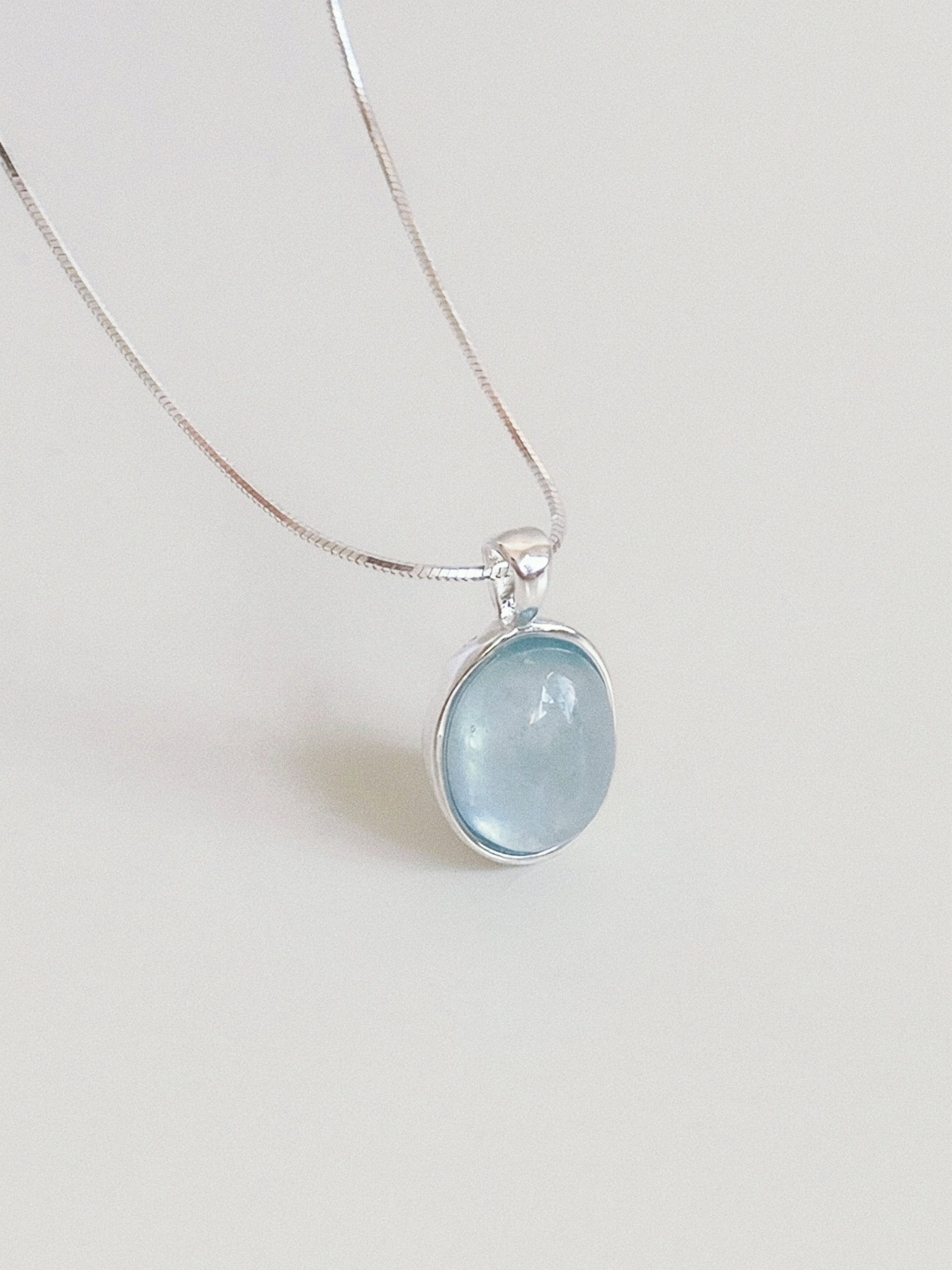 Natural aquamarine oval cabochon pendant in a textured sterling silver bezel hanging on a fine round snake chain