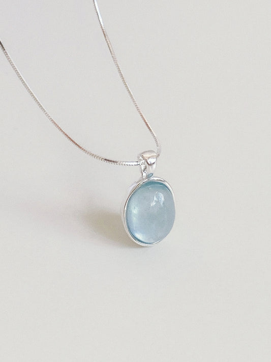 Natural aquamarine oval cabochon pendant in a textured sterling silver bezel hanging on a fine round snake chain
