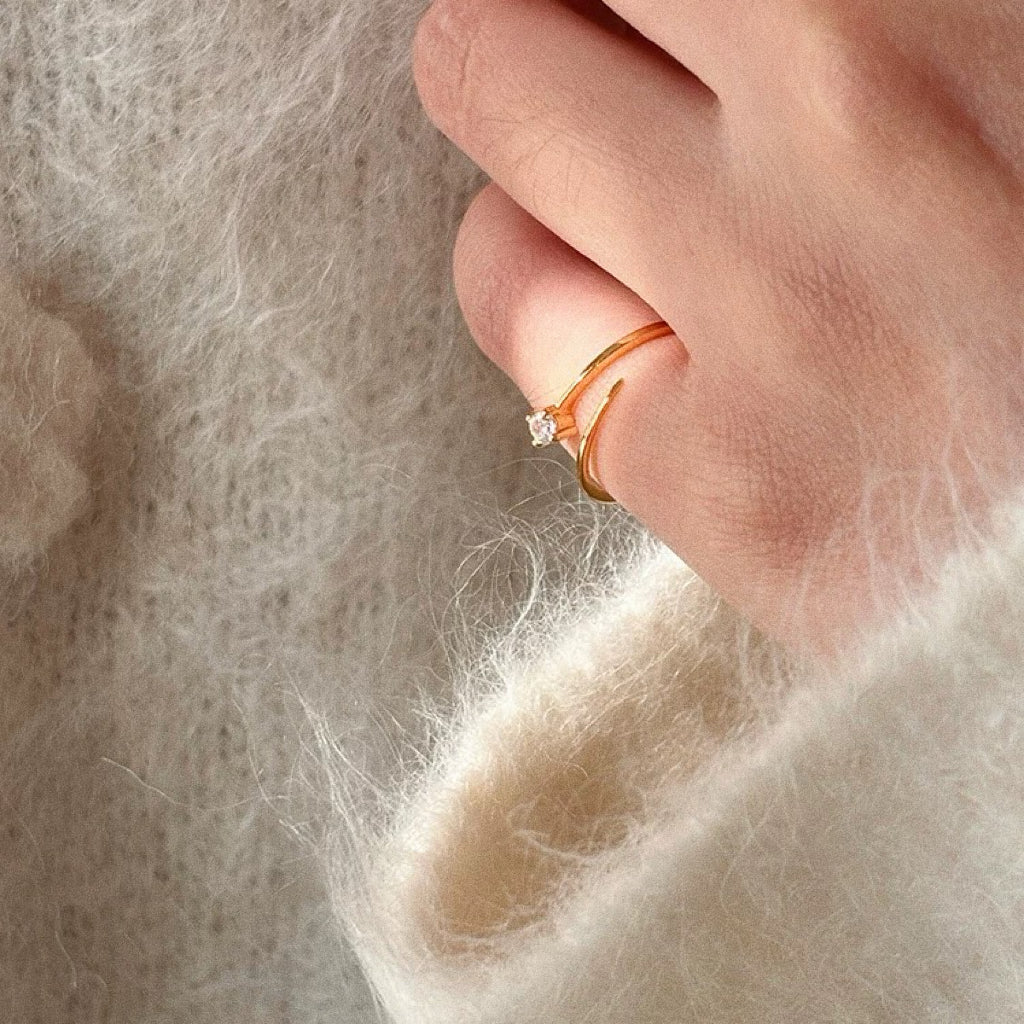 Close-up of dainty 18k gold plated open pinky ring with one cubic zirconia on finger against fluffy cream knit sleeve