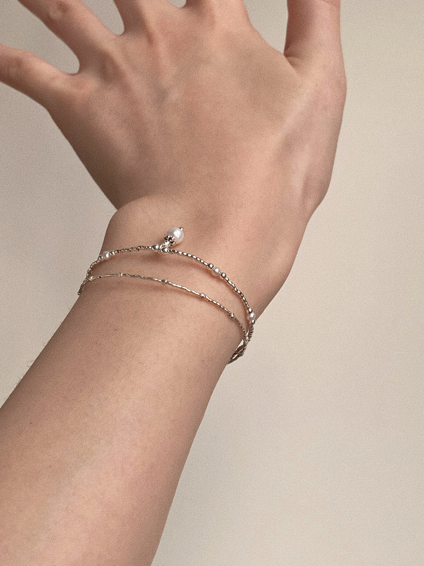 A woman wearing the structured double-layer pearl and silver bracelet, showing its clean silhouette.