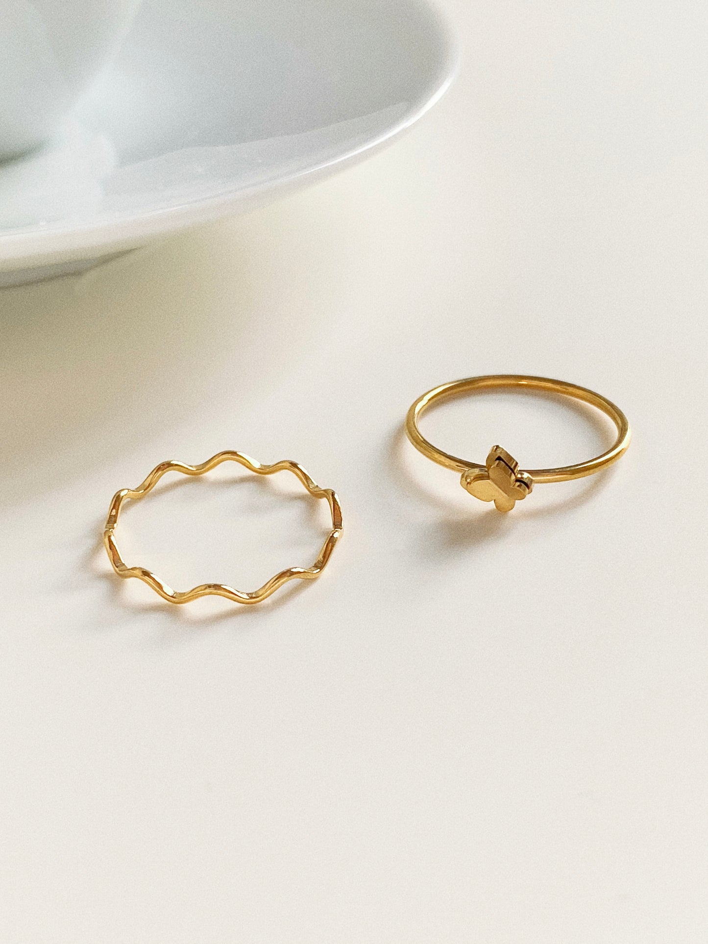 A lifestyle flat lay showing the gold Ocean Ripple wave ring next to a dainty gold butterfly charm ring.