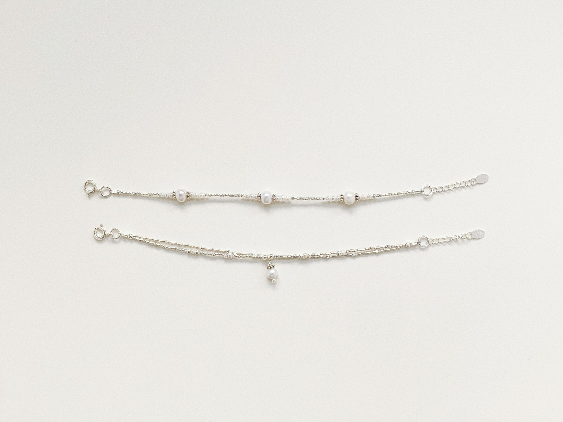 Comparison view of two delicate silver and pearl bracelets, showing the unique structured design.
