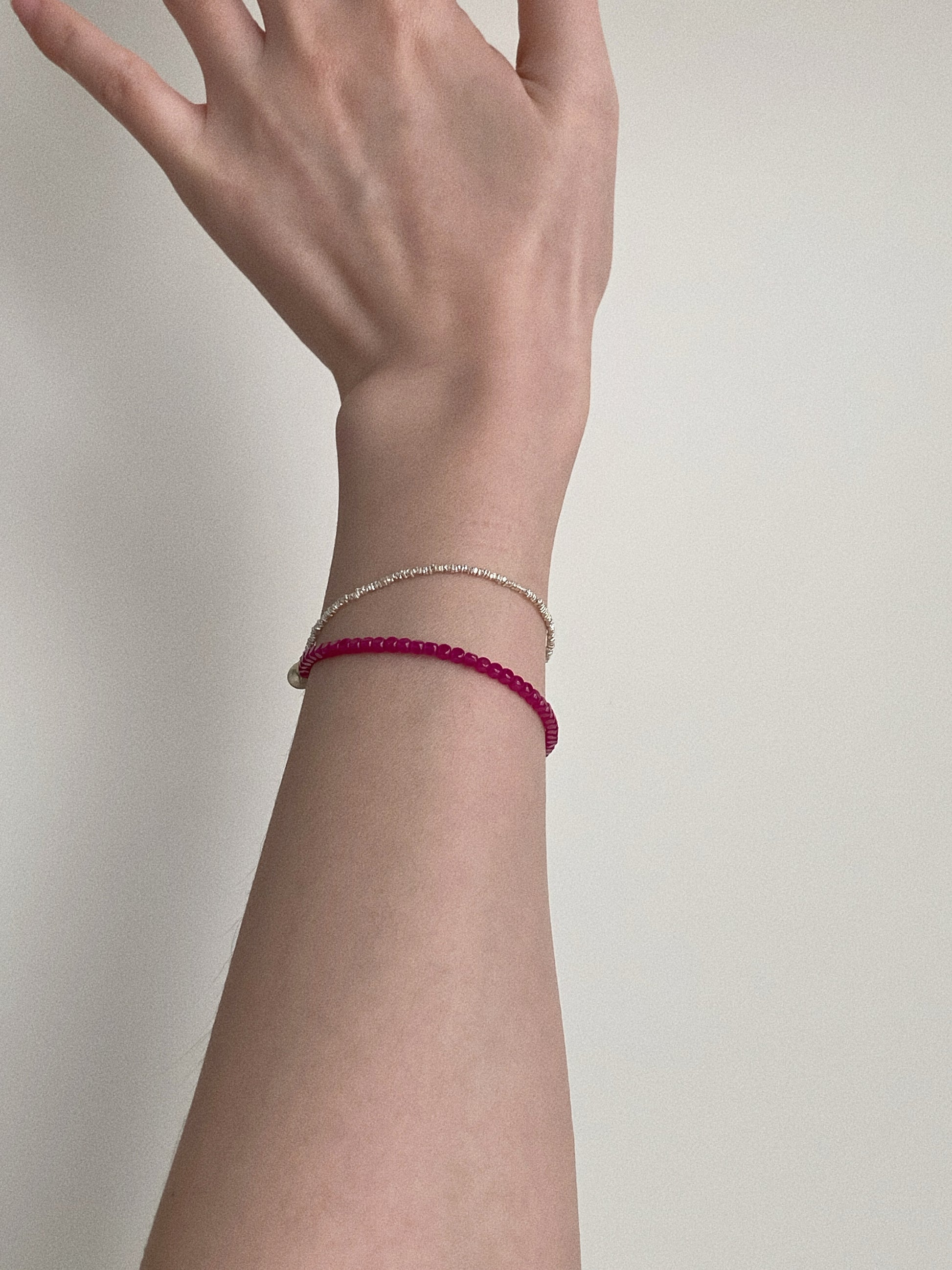 A woman’s wrist wearing a delicate double-layer red gemstone and silver bead bracelet against a neutral background.