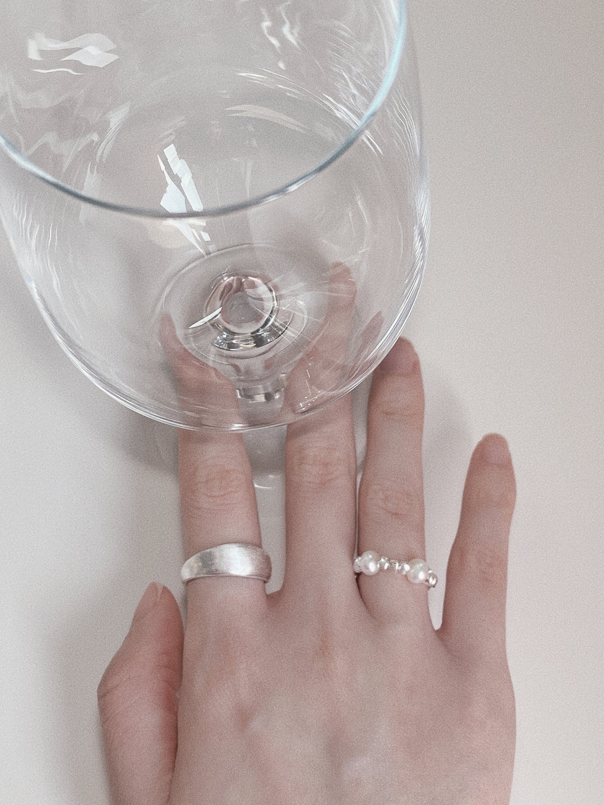 Close-up of a hand wearing the Mellow brushed dome ring alongside a dainty pearl bead ring, styled with a clear glass.