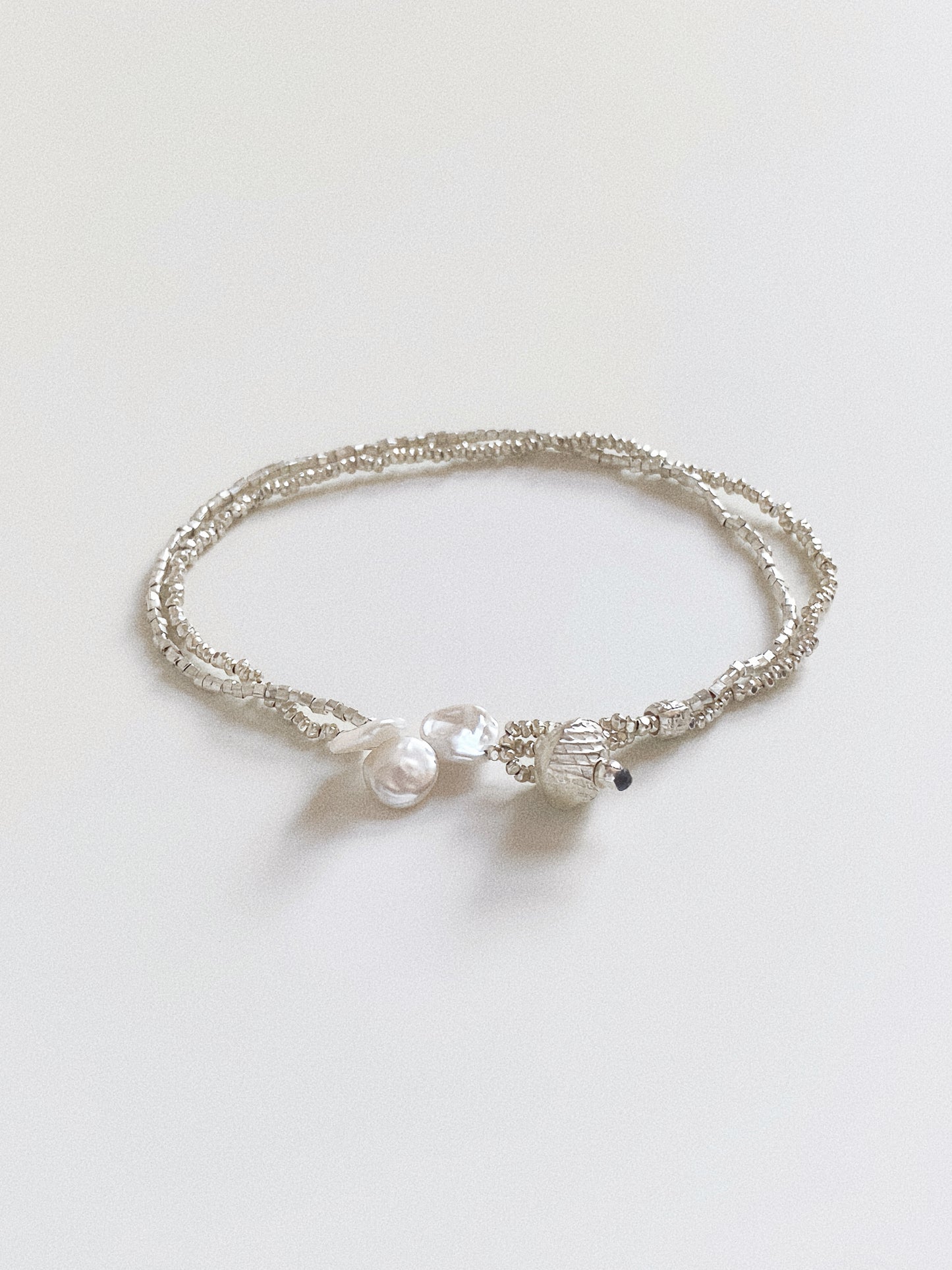Minimalist double row silver bracelet with pearl accents isolated on white background.