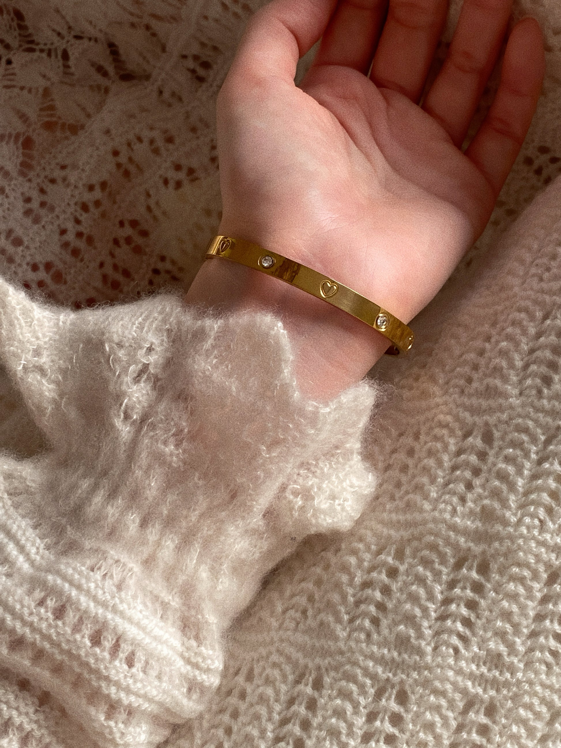 Model wearing the gold heart bangle solo with a cozy sweater, showing the fit on a small wrist.