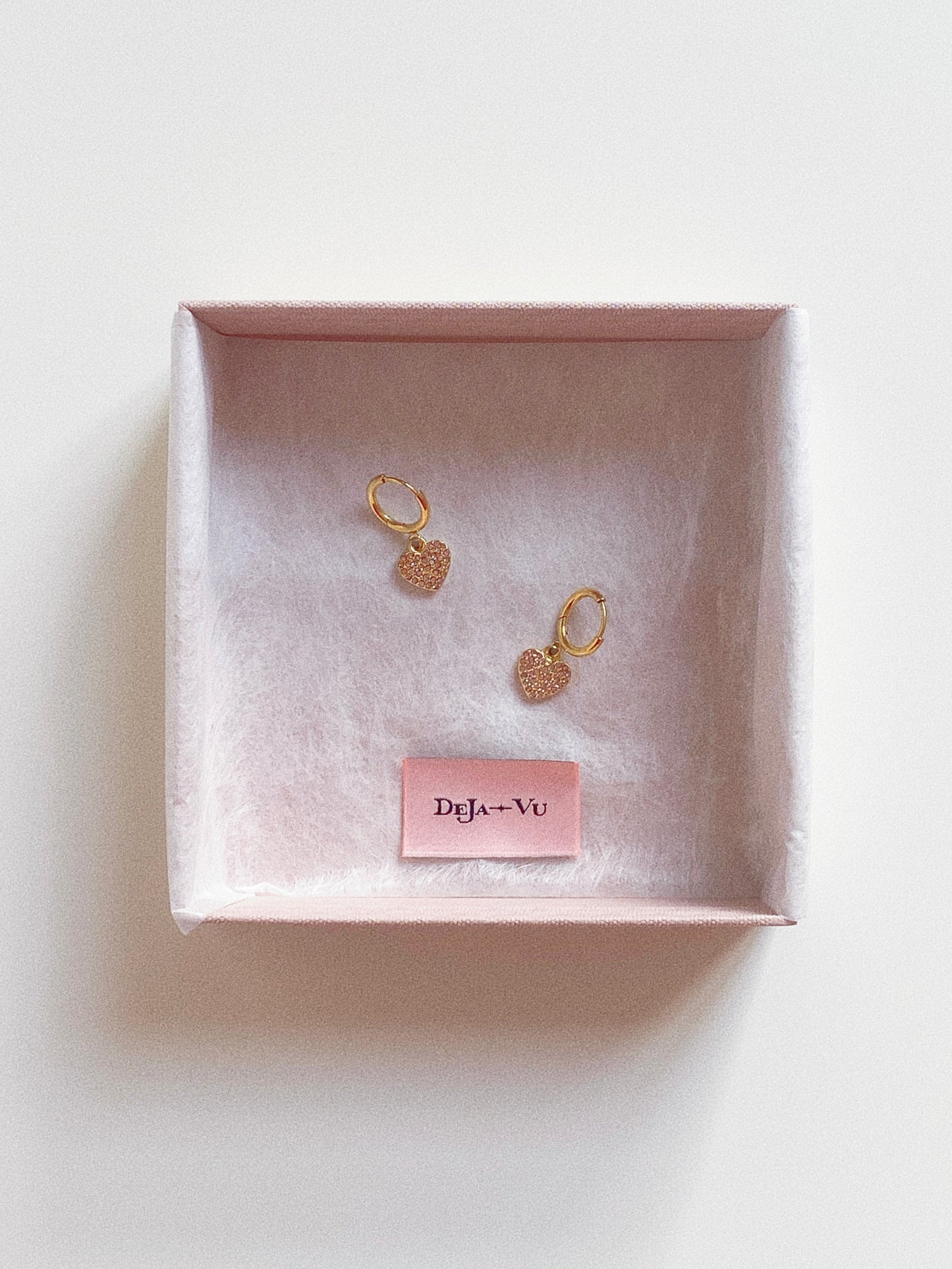 Pair of dainty gold heart hoops sitting inside a light pink Deja Vu jewellery box.