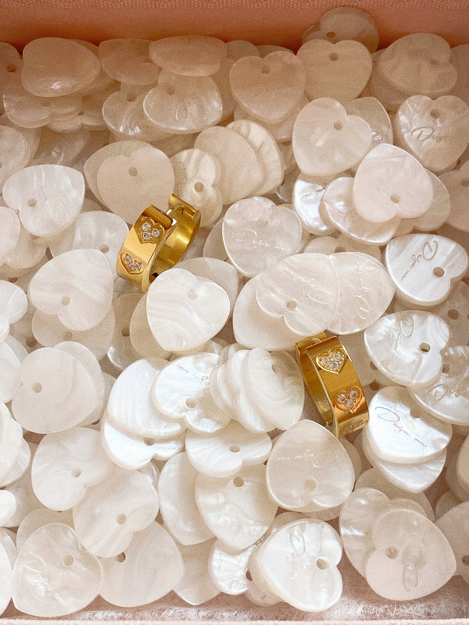 Close up of thick gold huggie earrings with heart details sitting inside a pink Deja Vu jewellery box.