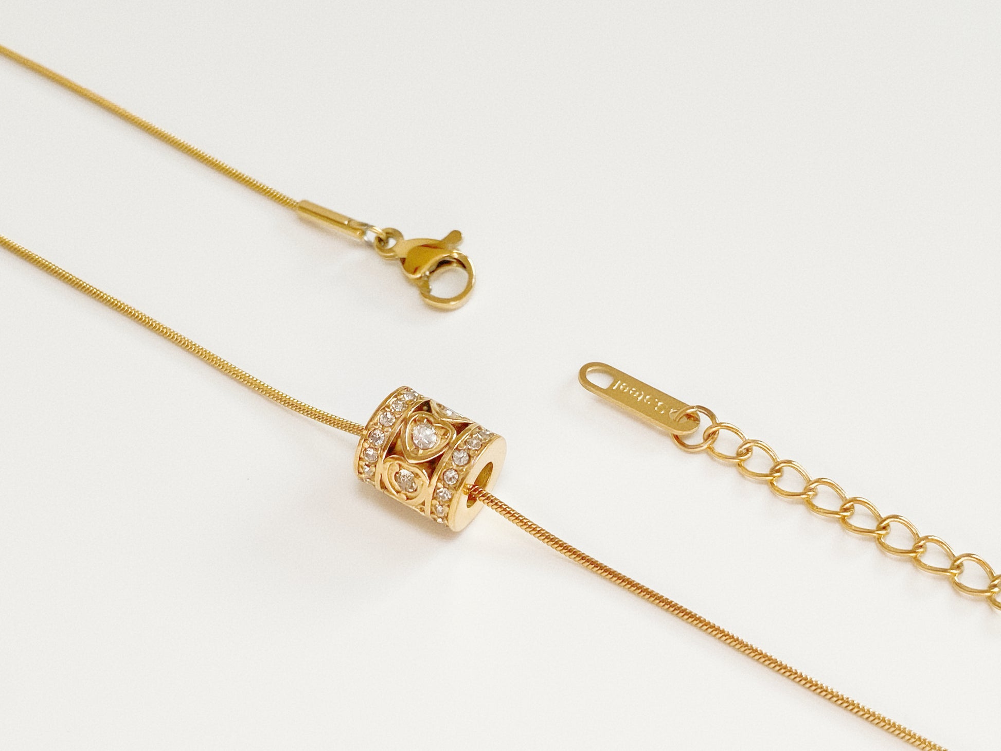 Detail shot of 18k gold plated stainless steel snake chain showing the lobster clasp and barrel charm.