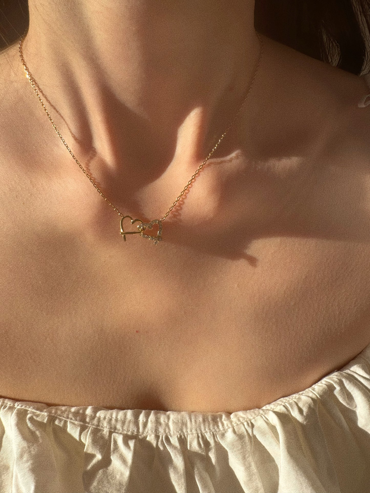 Model wearing gold interlocking heart necklace on collarbone, perfect Valentine's Day gift for her.