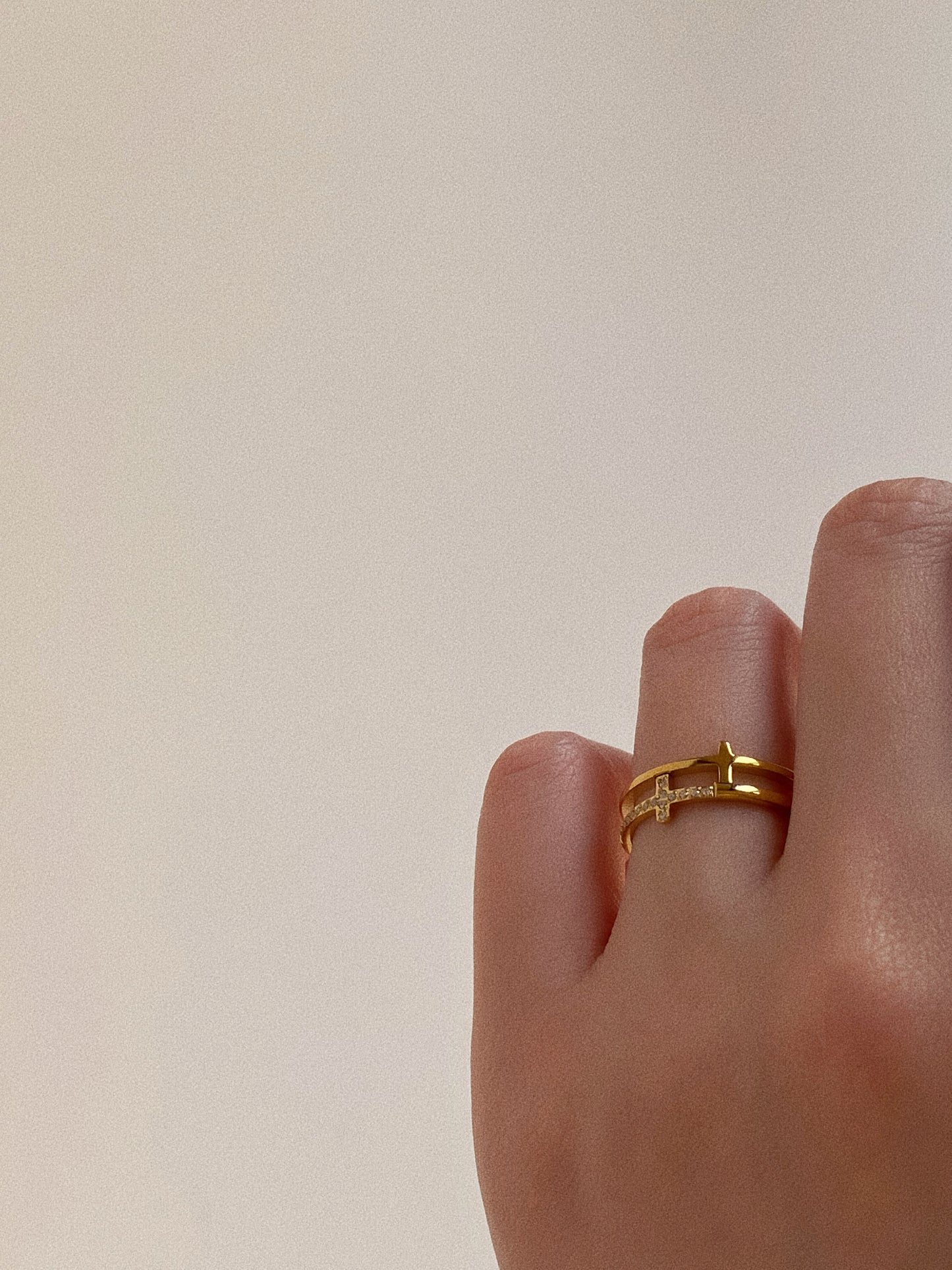 Woman's hand wearing a gold double band ring with a sideways crystal cross on the ring finger.