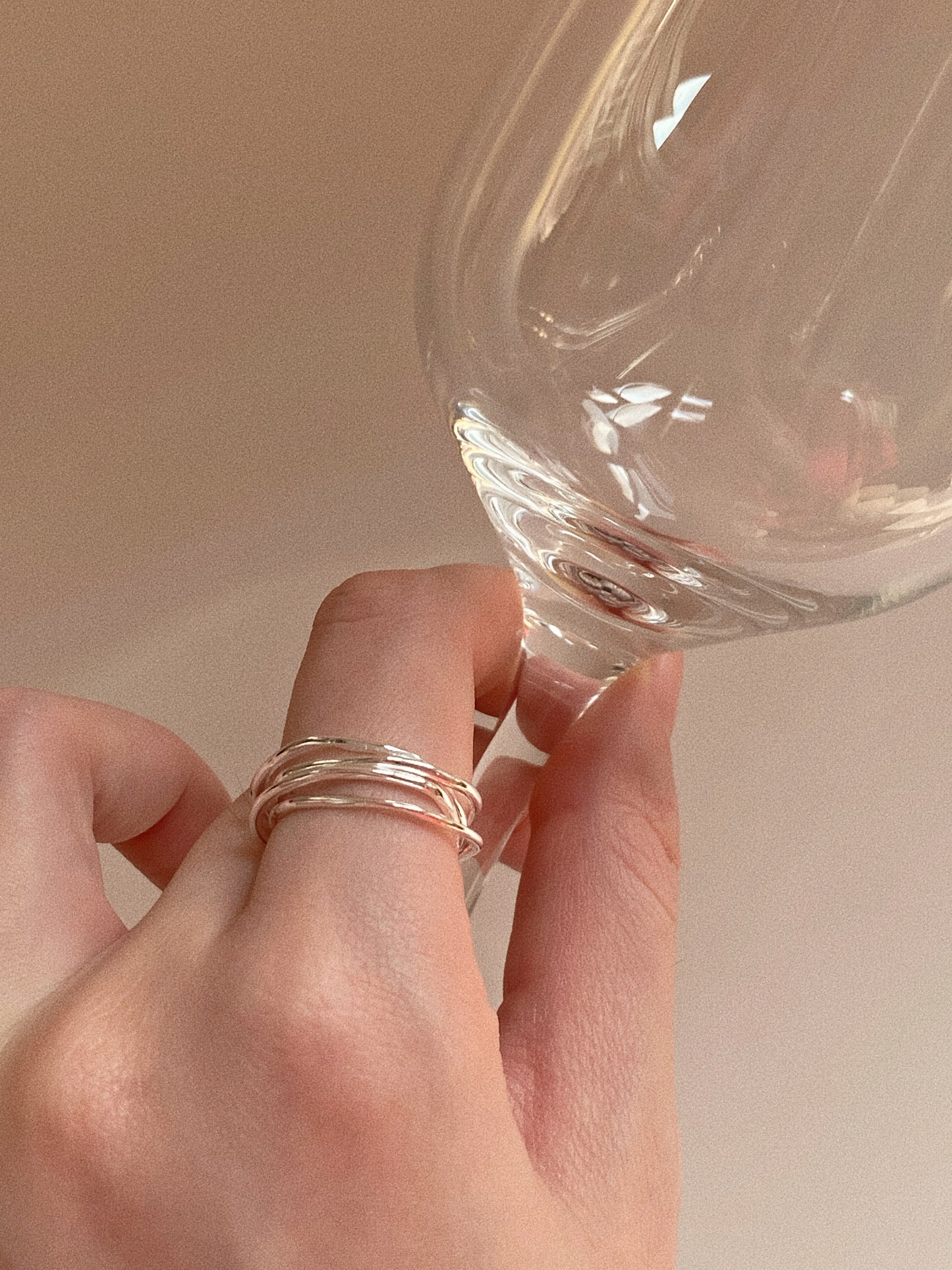 A person holding a wine glass, showcasing the modern silhouette of the double-layer silver knot ring.