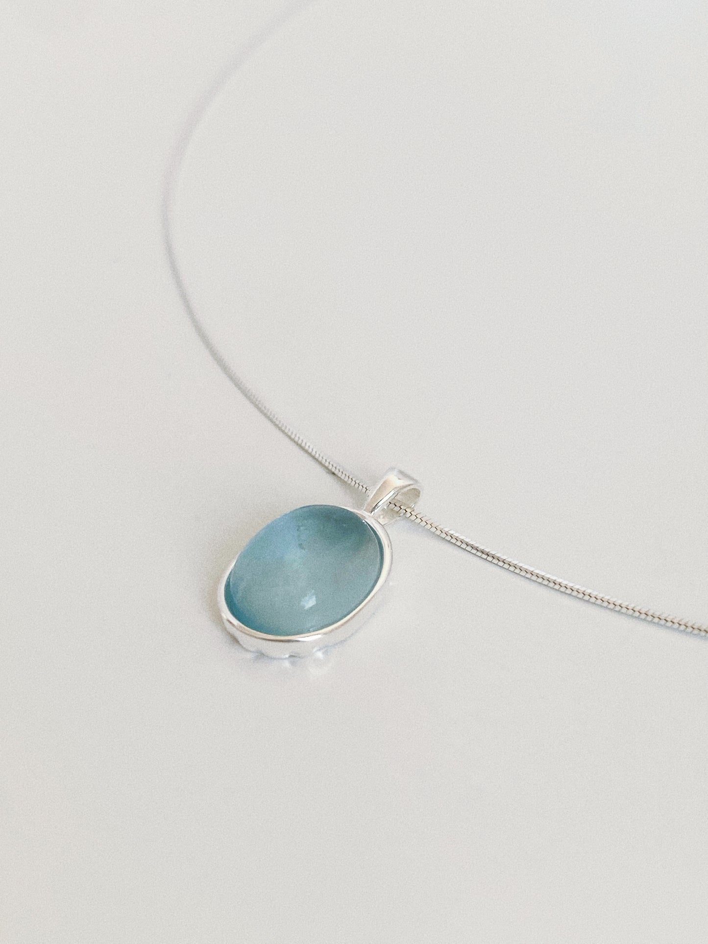 Angled close-up of a natural aquamarine pendant showing the domed cabochon, watery blue tone and hand-finished bezel