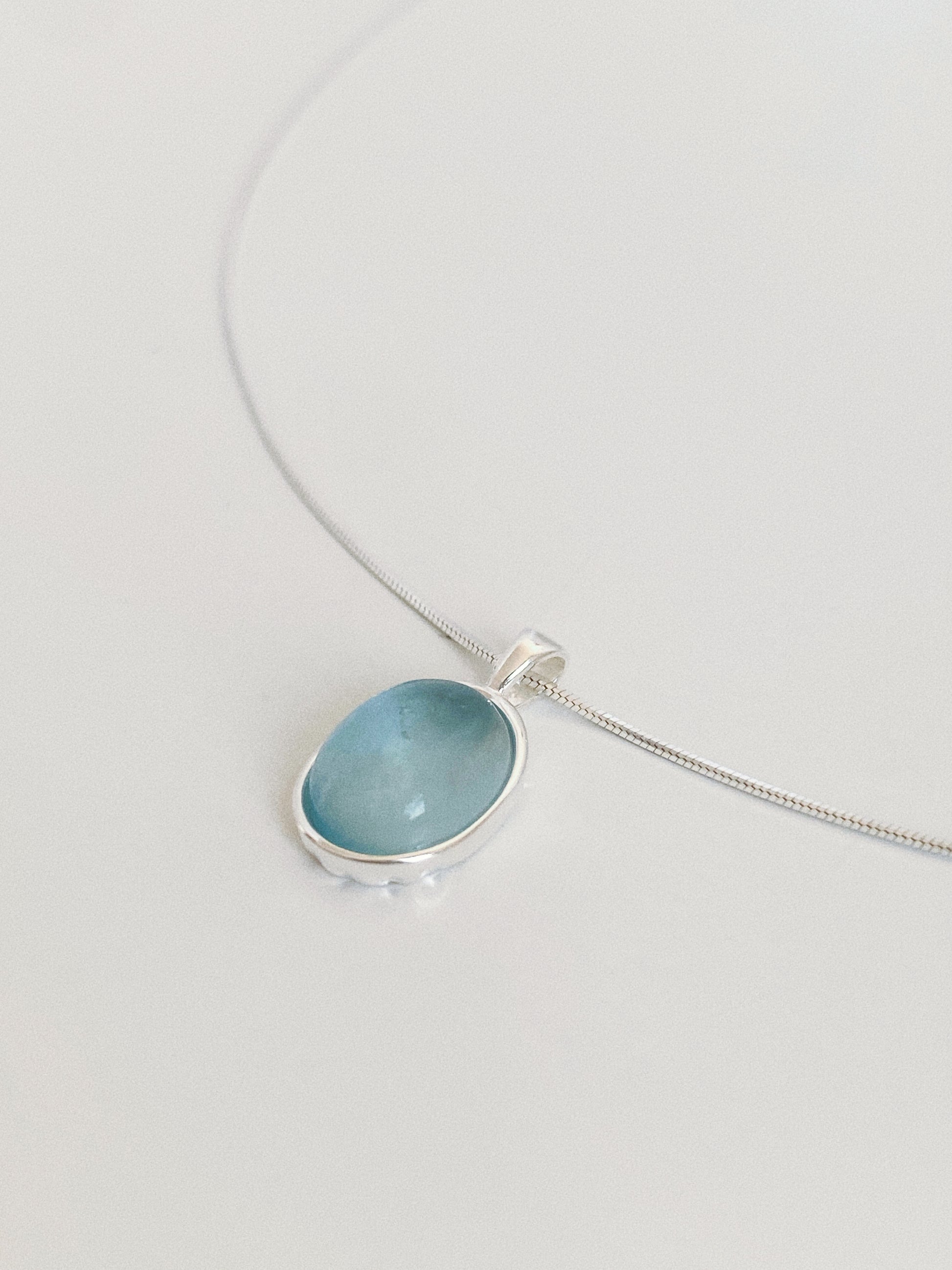 Angled close-up of a natural aquamarine pendant showing the domed cabochon, watery blue tone and hand-finished bezel