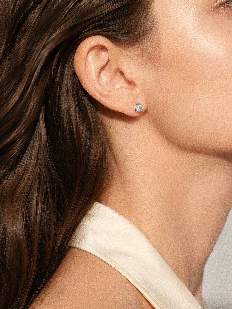 Natural blue topaz cabochon stud earring worn on model showing dainty 5-6mm size and soft pale blue colour