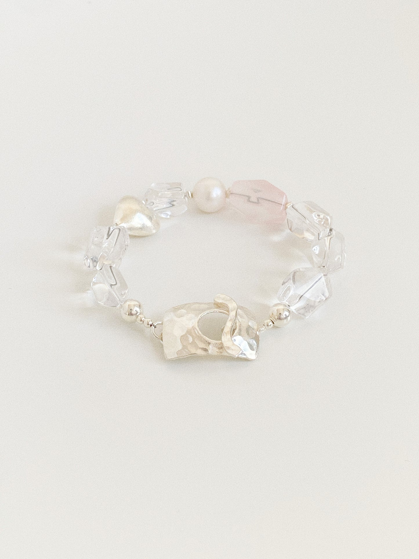 Angled view of a handmade natural crystal bracelet showing icy clear quartz nuggets, blush rose quartz and a freshwater pearl