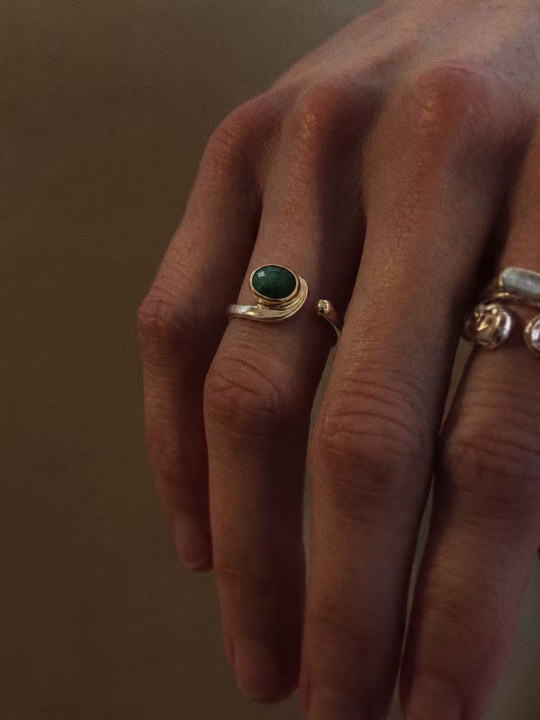 Natural emerald open ring worn on a finger, showing the oval green stone and curved silver band