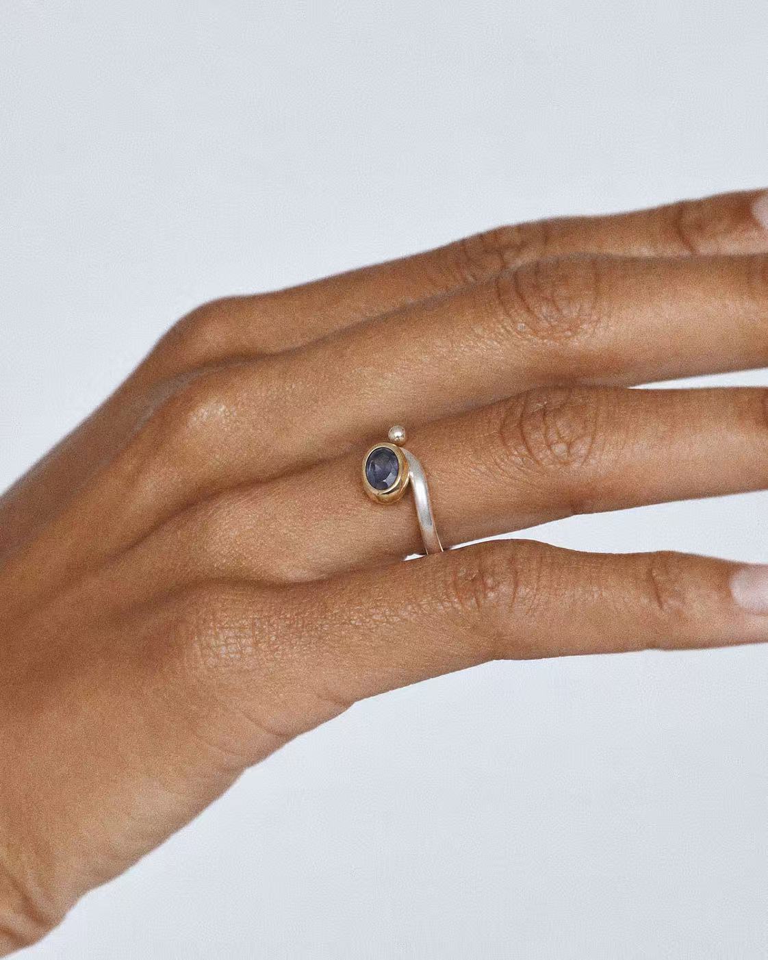 Natural iolite open ring worn on a finger, showing the oval gemstone and curved silver band