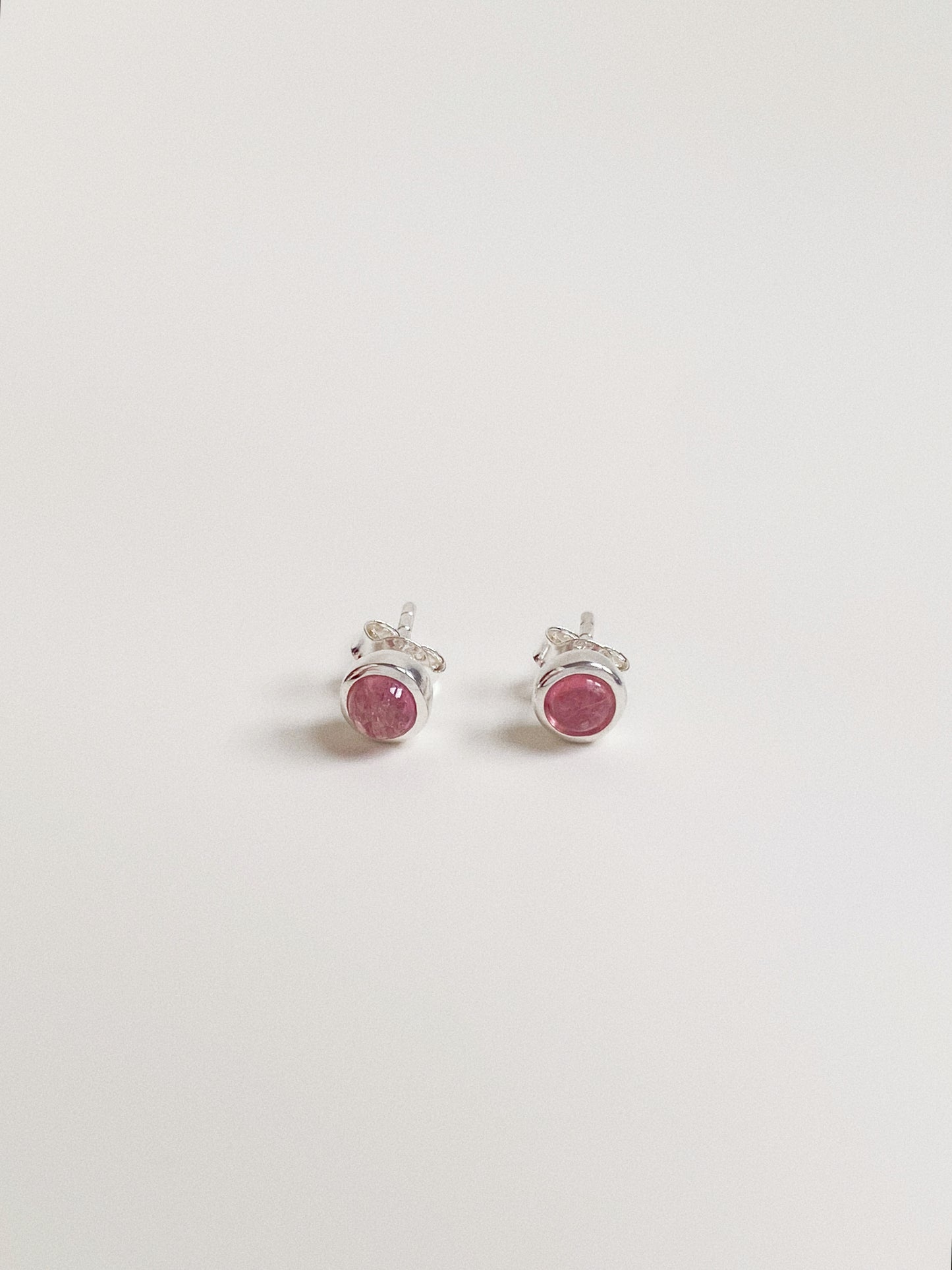 Pair of 5-6mm round natural pink tourmaline cabochon stud earrings in sterling silver bezel setting.
