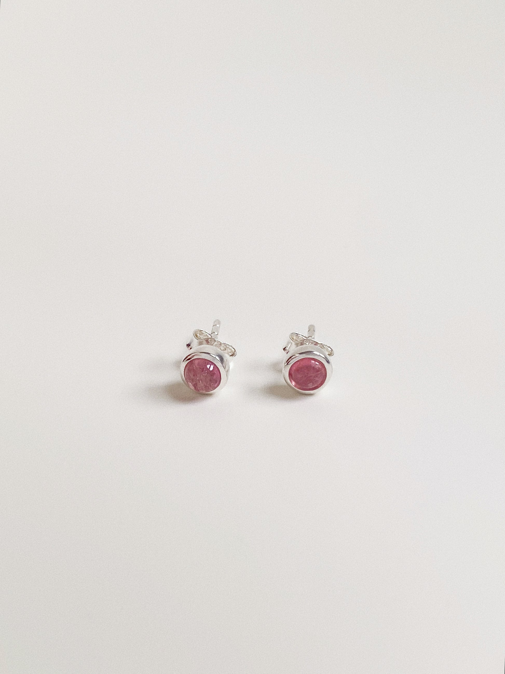 Pair of 5-6mm round natural pink tourmaline cabochon stud earrings in sterling silver bezel setting.