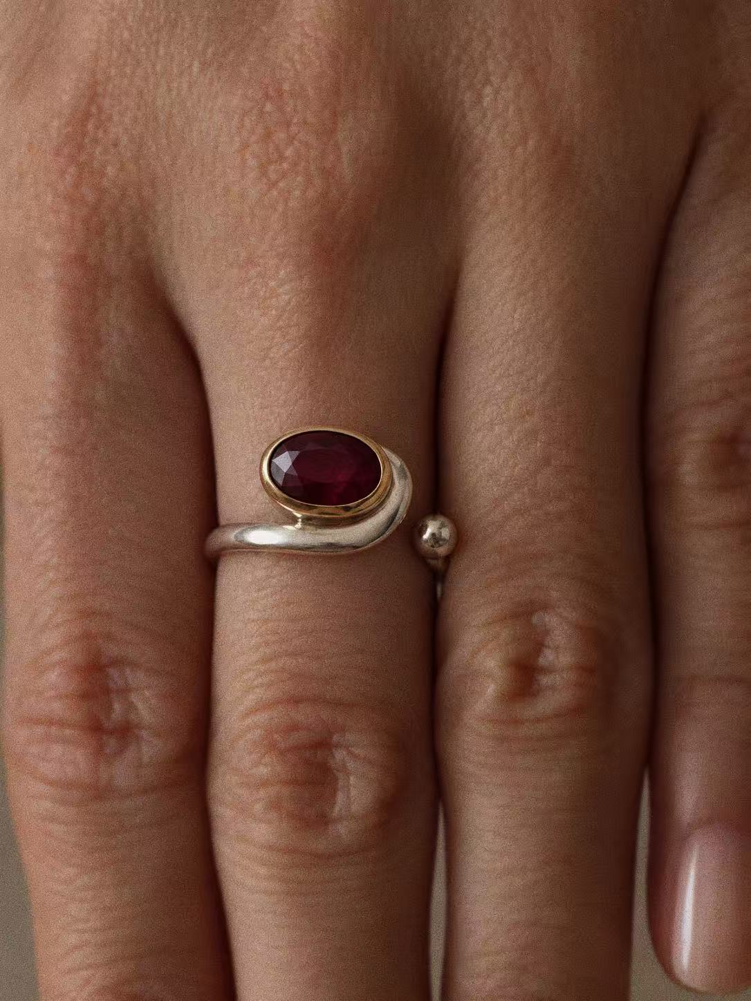 Natural ruby two-tone open ring worn on a finger, showing the oval stone and curved silver band