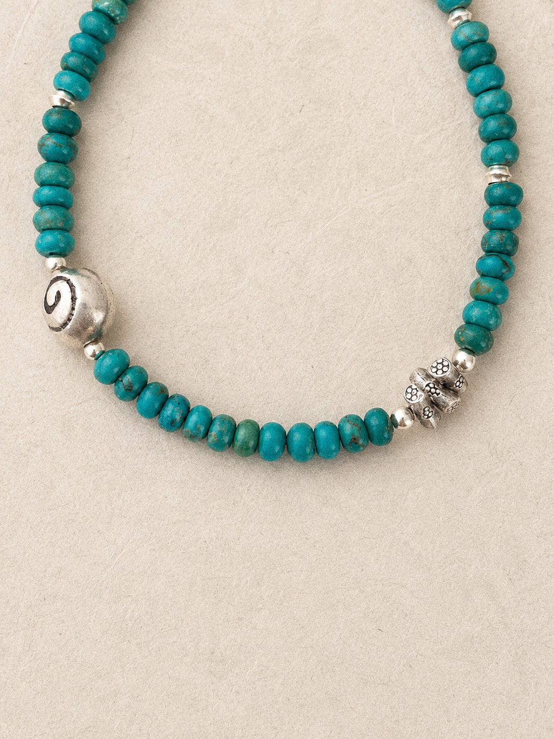 Close up of natural turquoise rondelle beads with matrix veining and a carved silver spiral bead