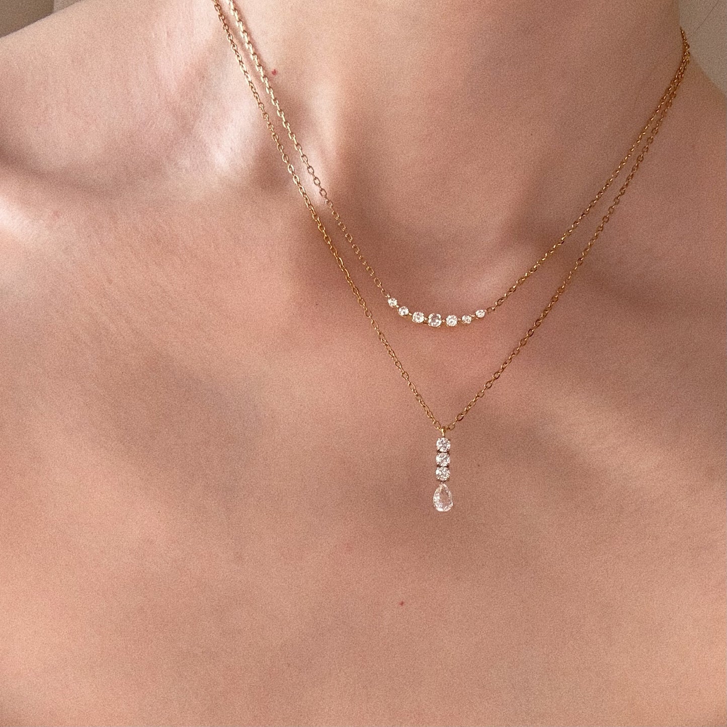 Model wearing a layered necklace stack: The Crystal Smile Bar Necklace (top) and The Vienna Teardrop Necklace (bottom).