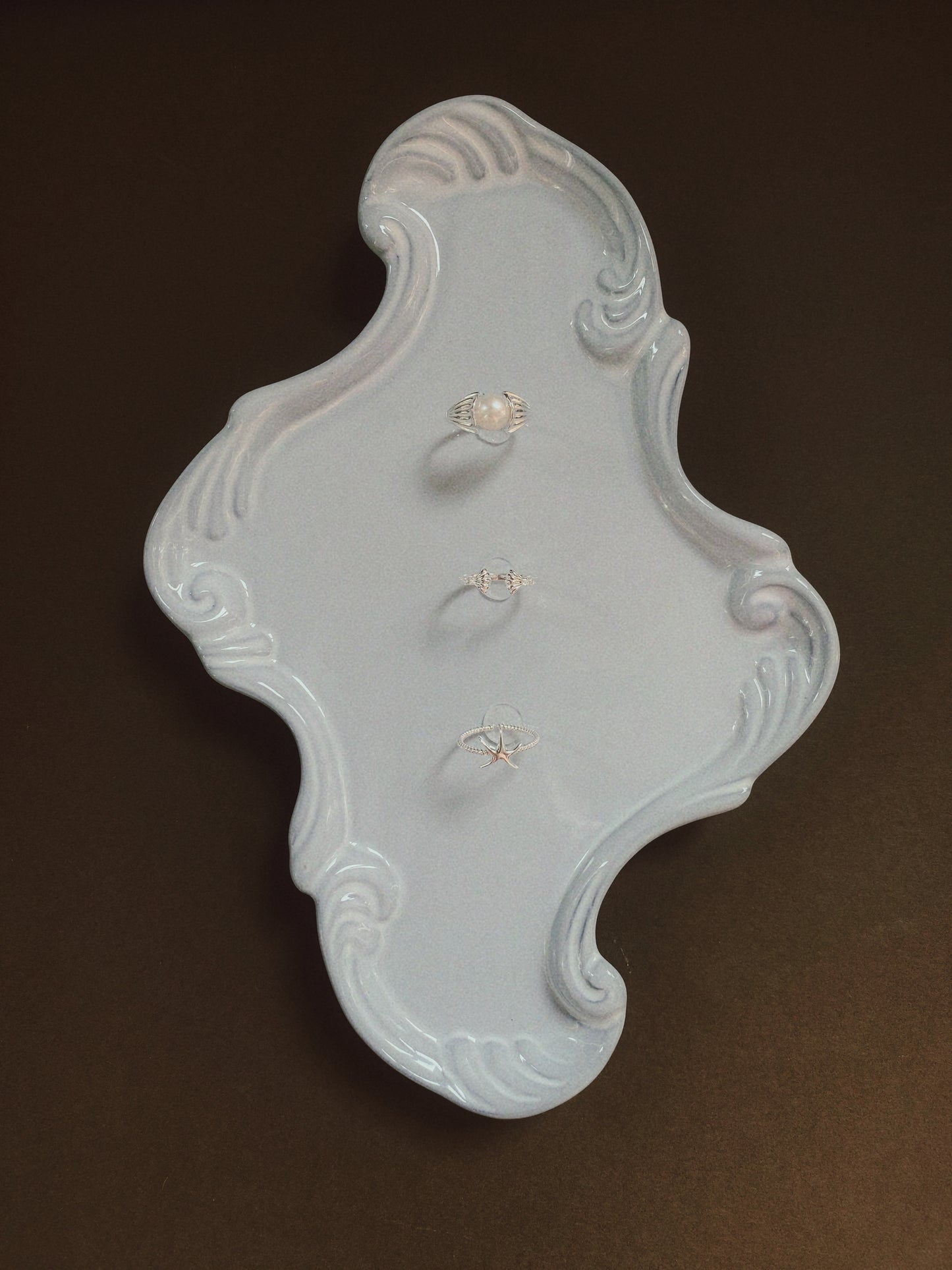 Three ocean-inspired silver rings displayed vertically on a decorative white ceramic tray against a dark brown background.