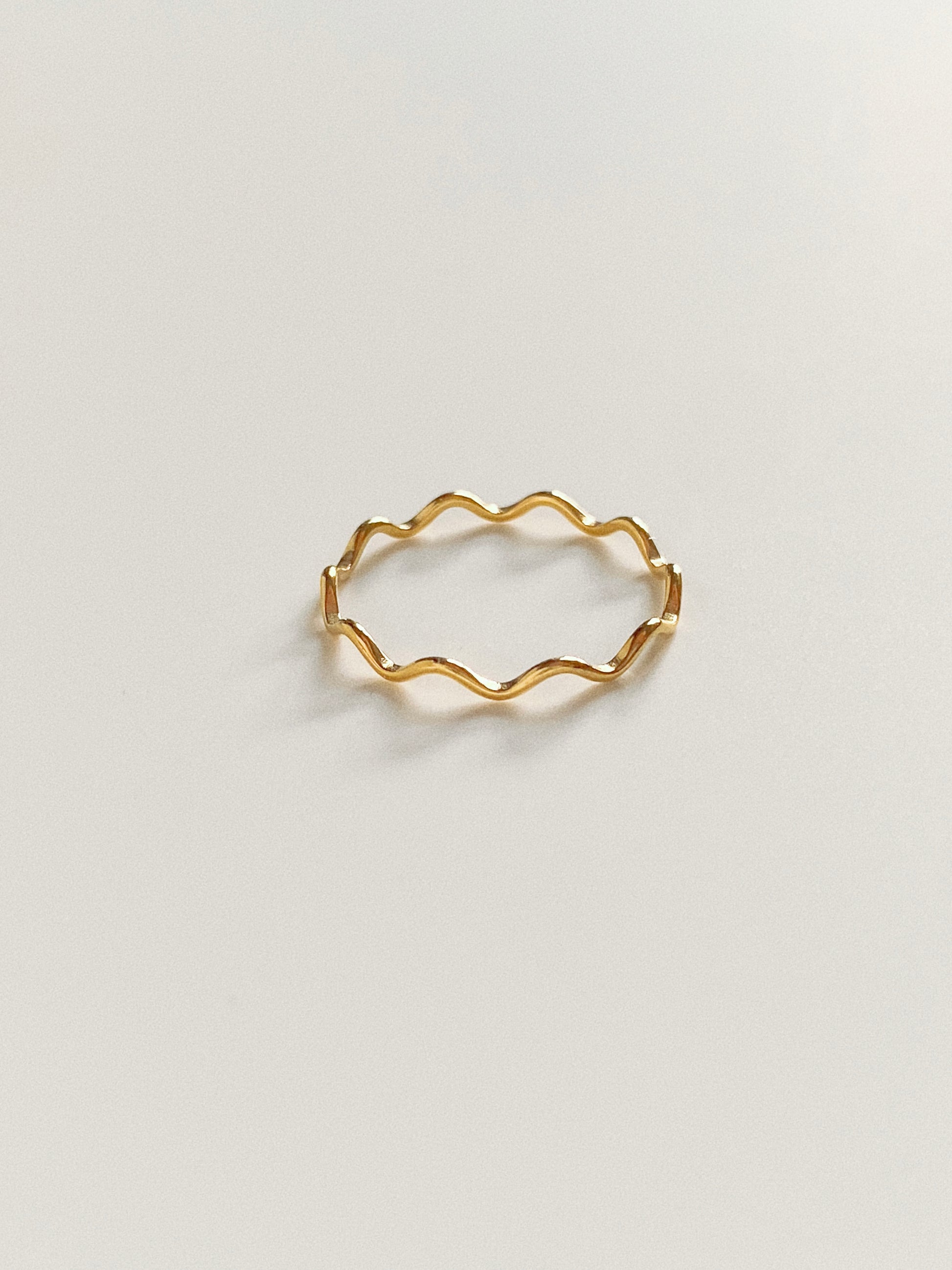 A high-angle shot of a slender, wavy-shaped gold ring made of durable titanium steel on a clean white background.