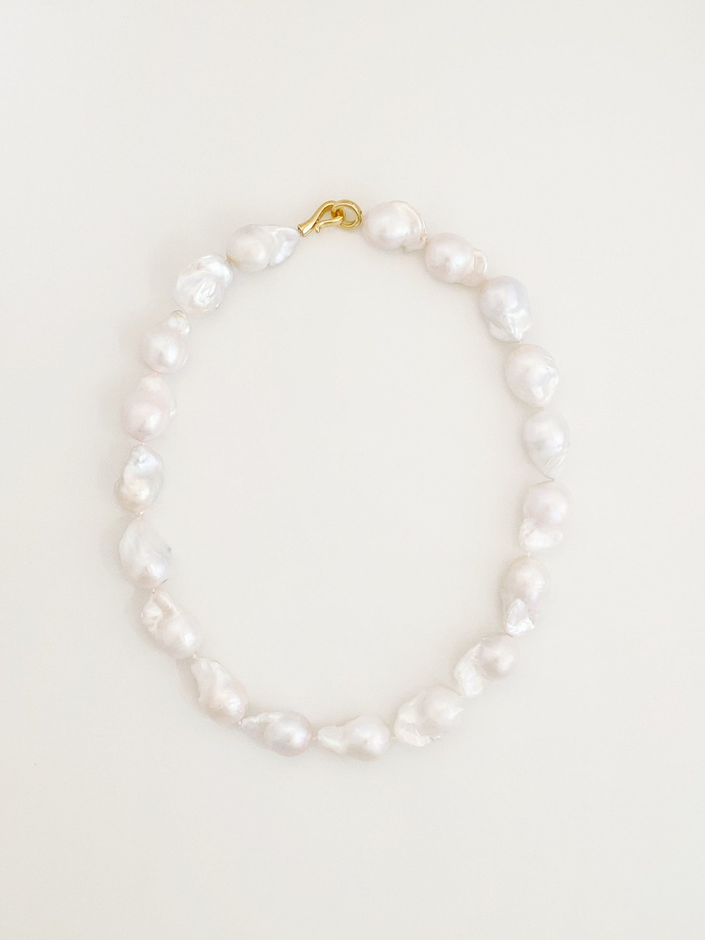 Statement strand of large natural fireball baroque freshwater pearls with a sculptural 14k gold S-hook clasp, laid flat in a circle