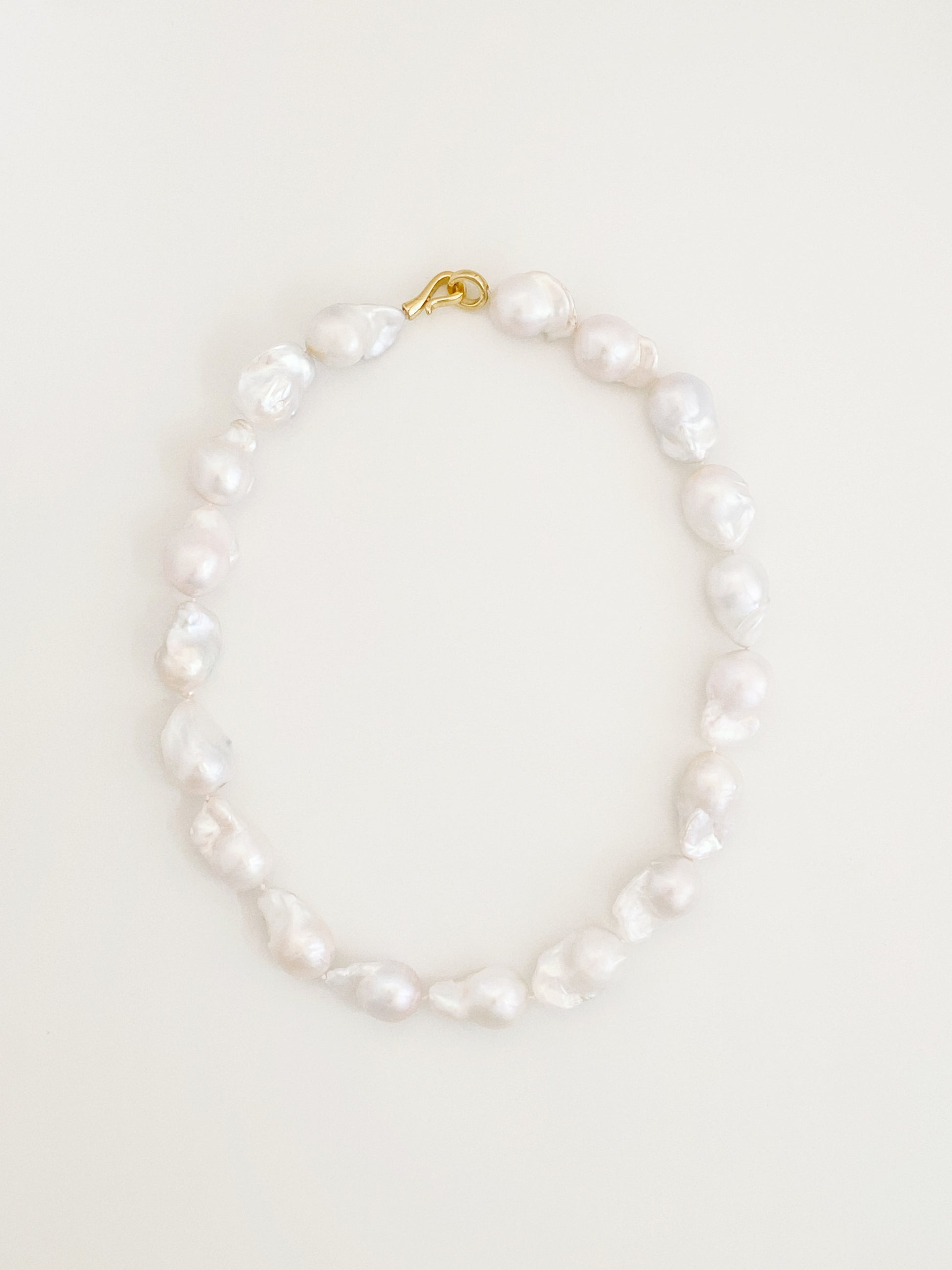 Statement strand of large natural fireball baroque freshwater pearls with a sculptural 14k gold S-hook clasp, laid flat in a circle