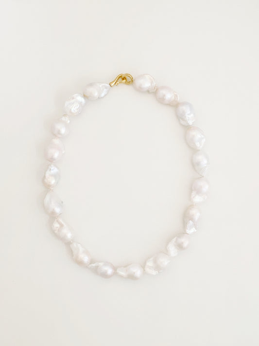 Statement strand of large natural fireball baroque freshwater pearls with a sculptural 14k gold S-hook clasp, laid flat in a circle