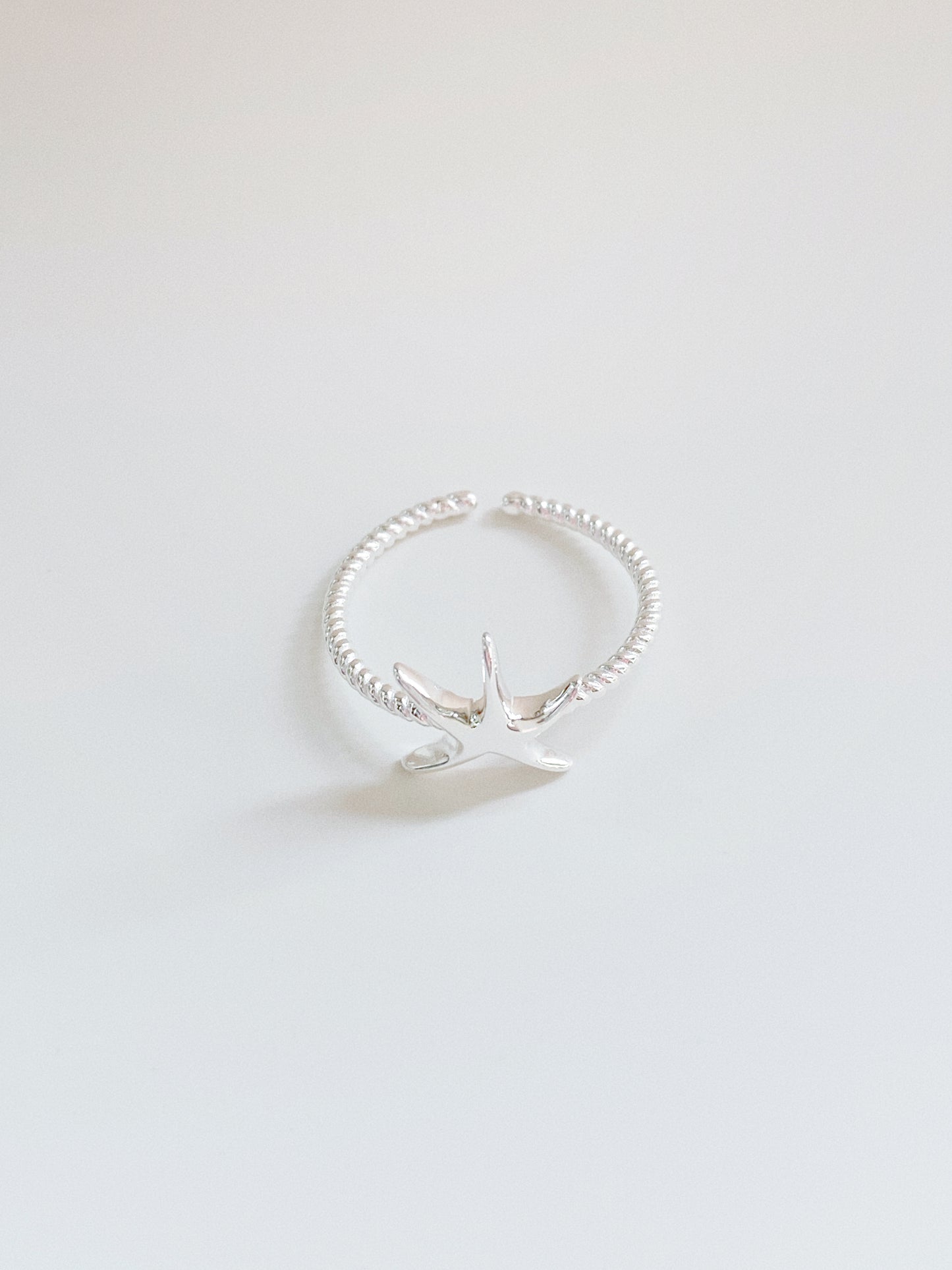 High-angle shot of a dainty 925 sterling silver starfish ring with a twisted rope-style band on a clean white background.