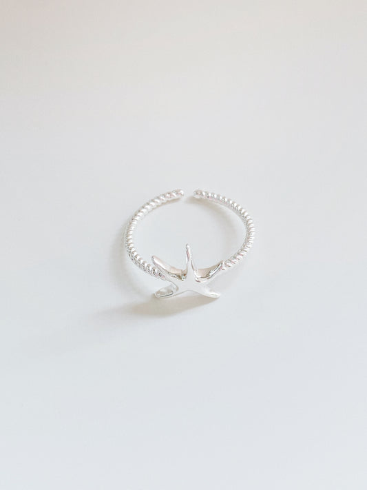 High-angle shot of a dainty 925 sterling silver starfish ring with a twisted rope-style band on a clean white background.