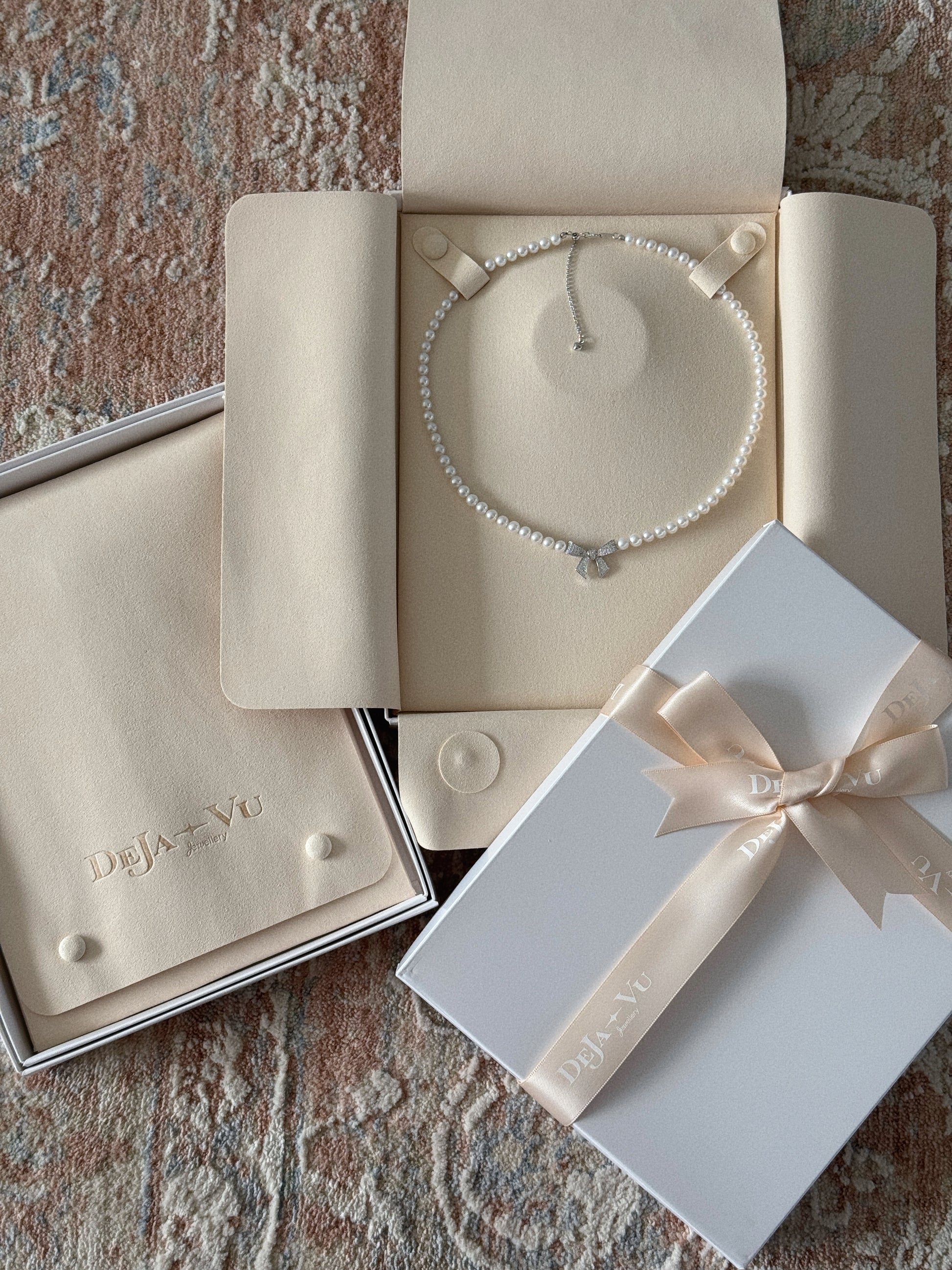 Pearl bow necklace displayed in a Deja Vu suede jewellery folder with white gift box and satin ribbon