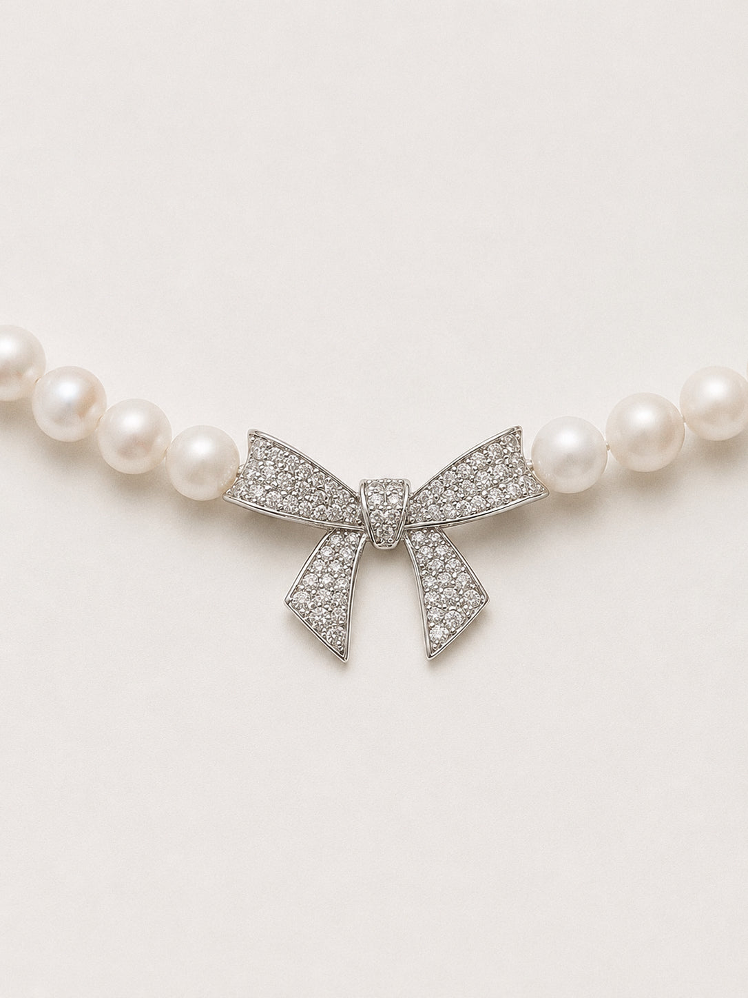 Close up of the pavé crystal bow centrepiece set between white pearls on the bow pearl necklace