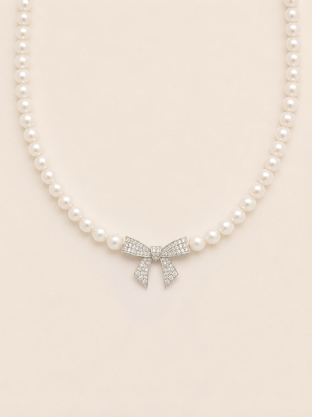 Pearl bow necklace with a full strand of white pearls and a pavé crystal bow sitting at the centre