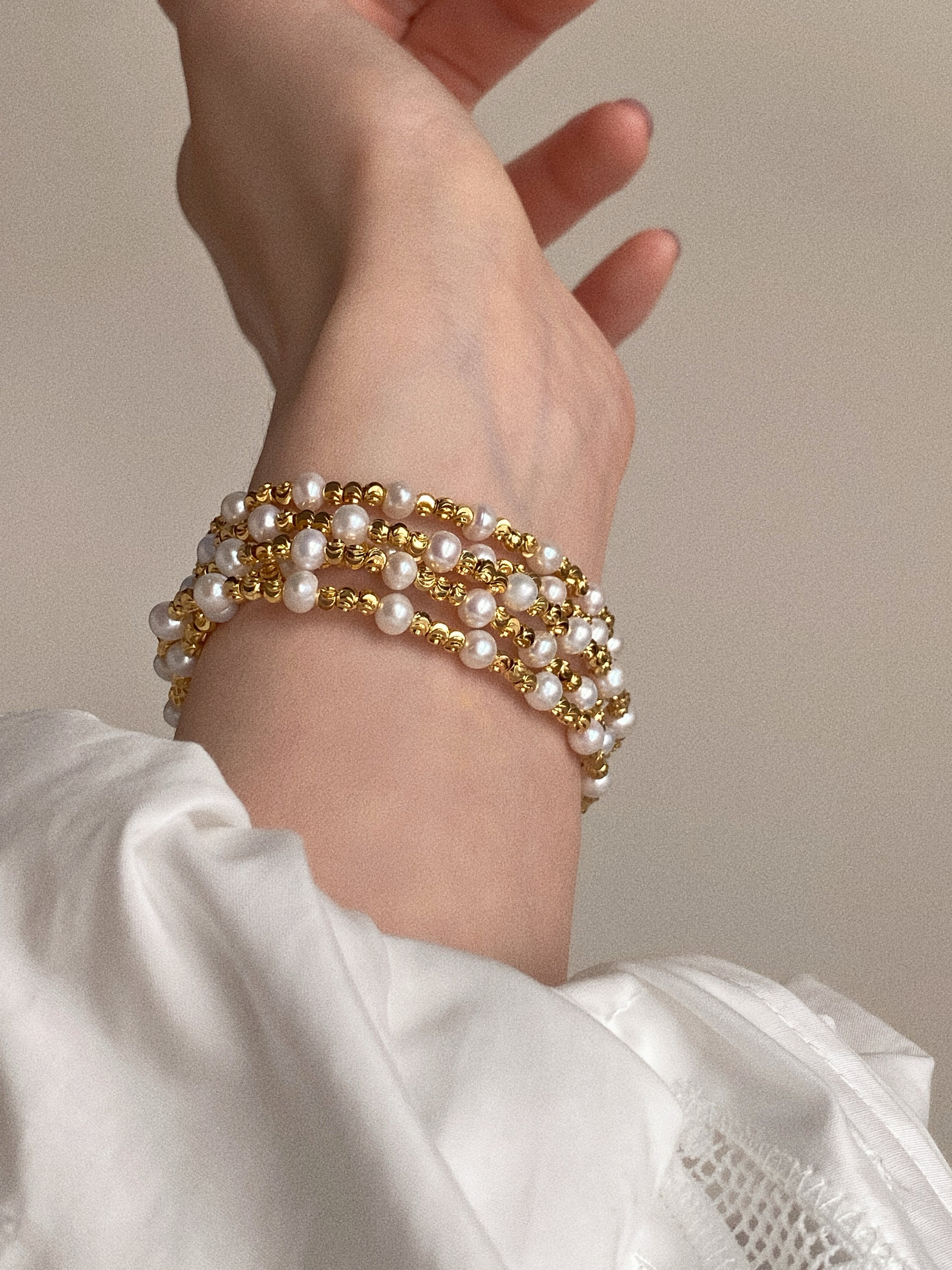 Close-up of pearl and diamond-cut gold bead necklace worn as a multi-layer wrap bracelet