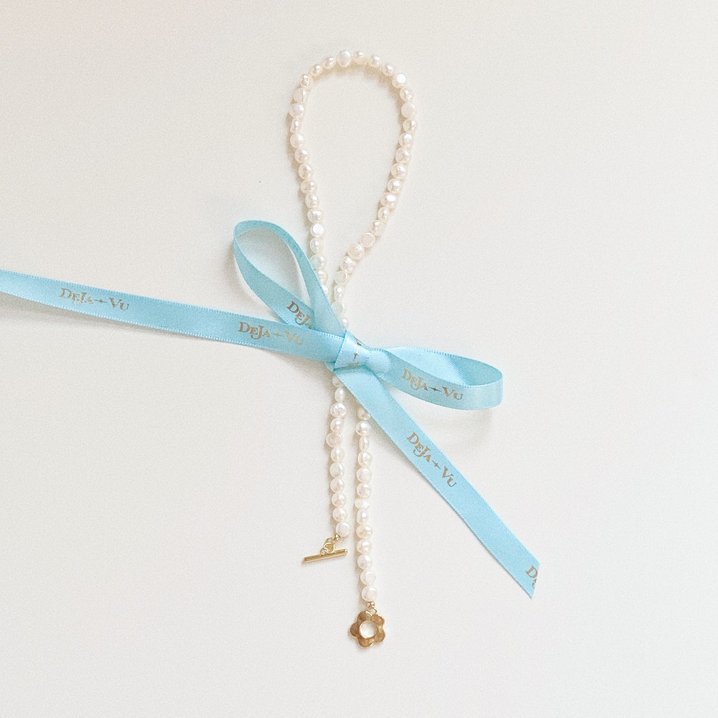 Freshwater pearl strand styled with turquoise Deja vu ribbon tied in a bow next to flower toggle clasp