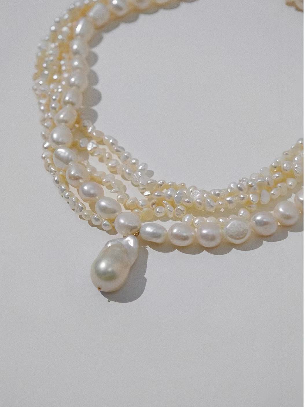 White handcrafted pearl necklace with 5 layers of beads cascading down to a central pearl drop.