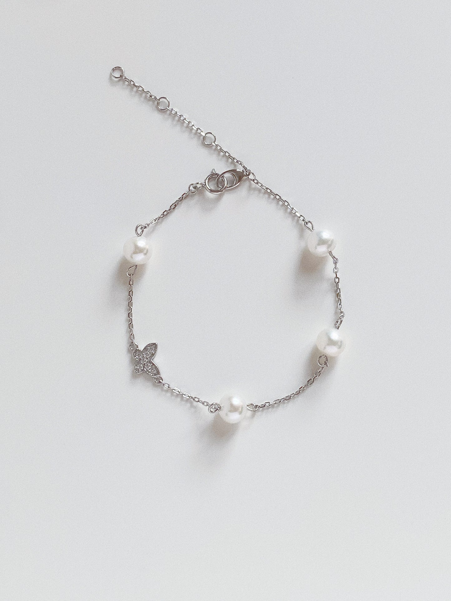 Flat lay of 925 sterling silver station bracelet featuring spaced out natural freshwater pearls and a crystal butterfly charm.
