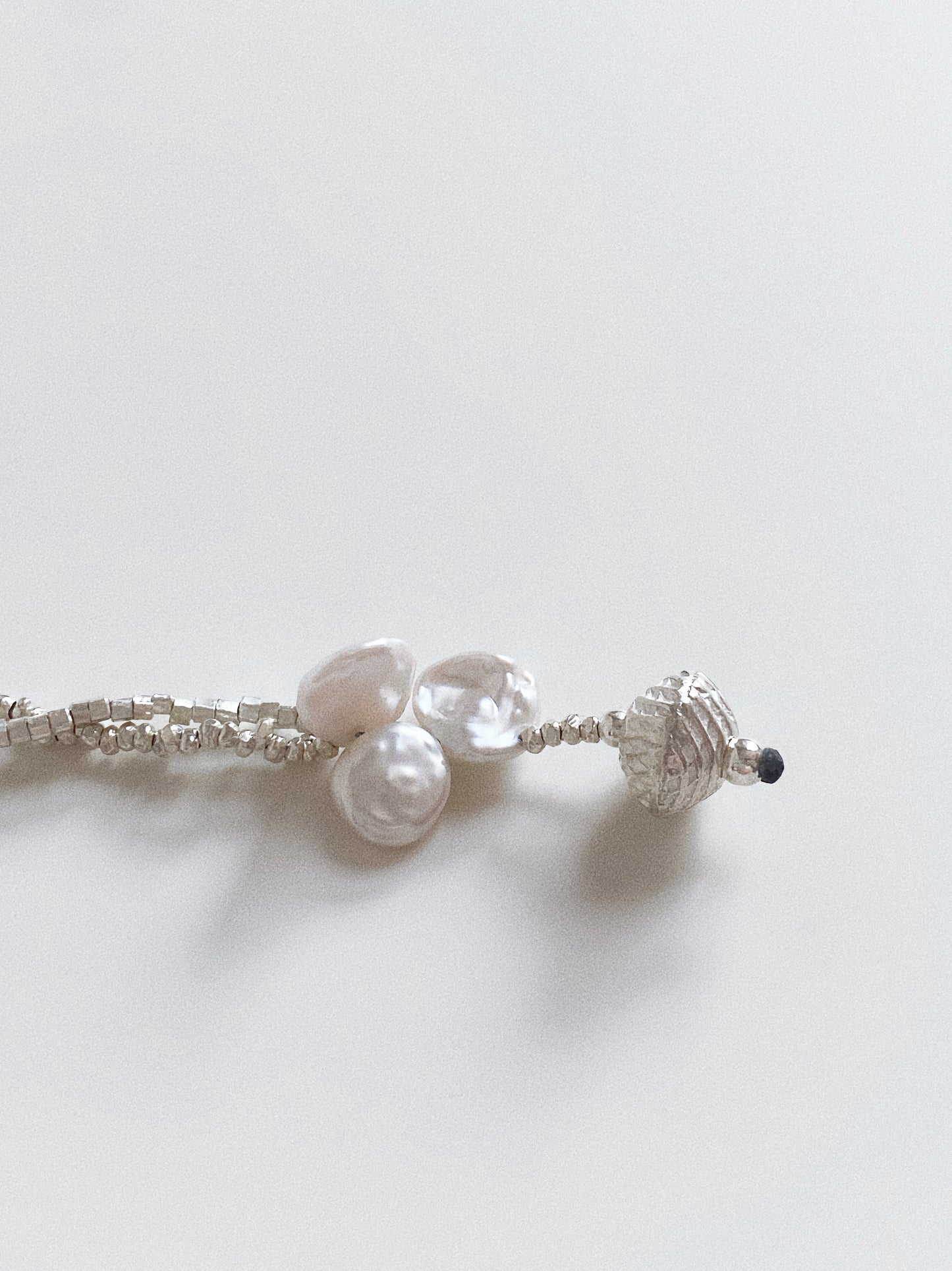 Close up of natural Baroque Keshi pearls and textured silver charm on a double strand silver bracelet.