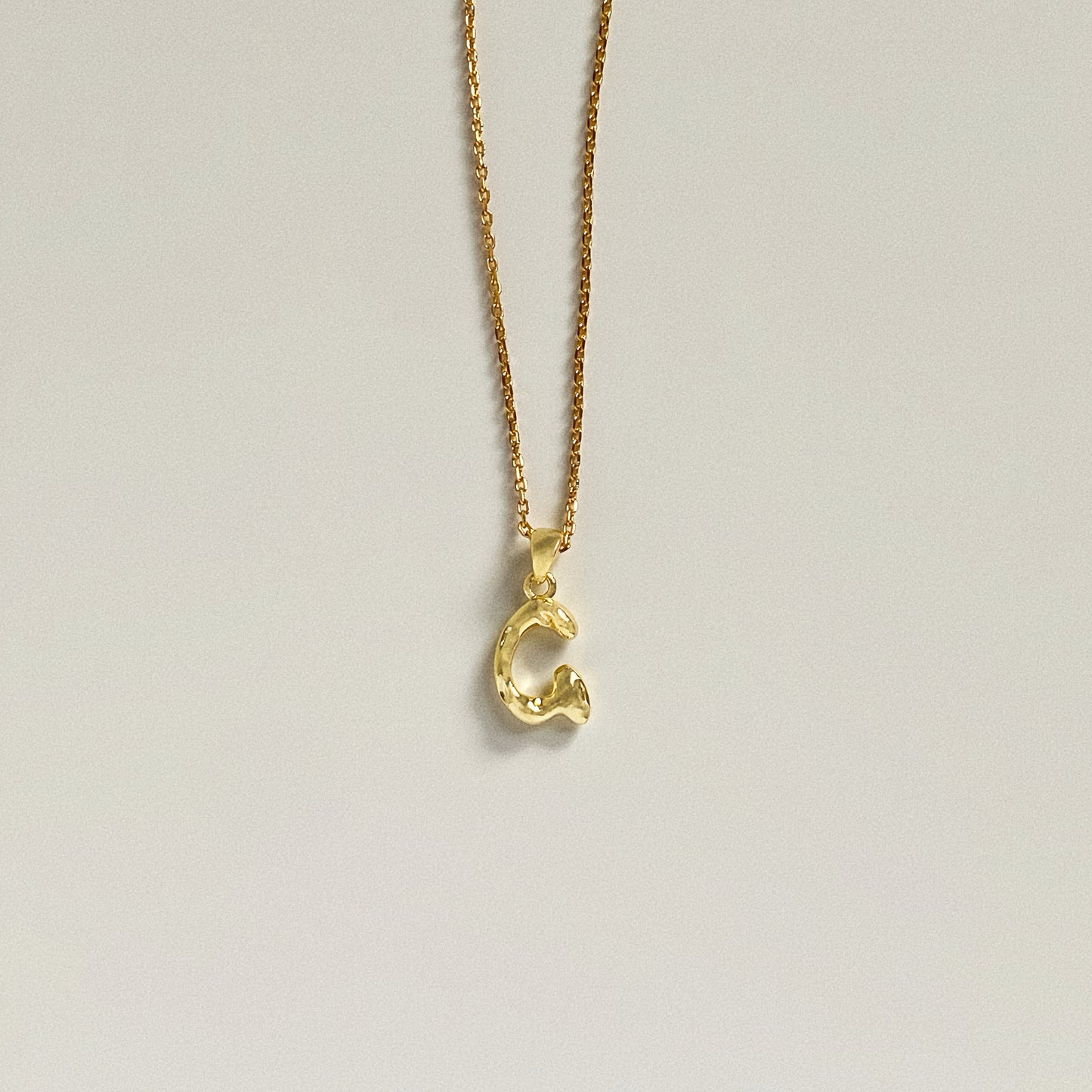Dainty gold initial necklace featuring a bubble font letter G pendant on a thin cable chain.