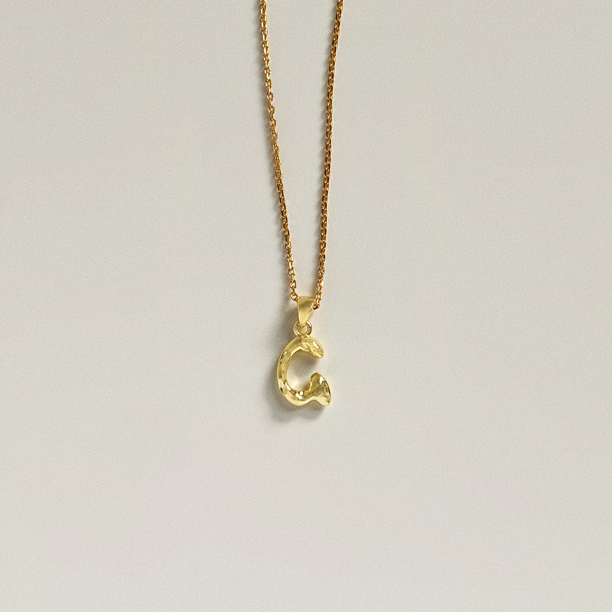 Dainty gold initial necklace featuring a bubble font letter G pendant on a thin cable chain.