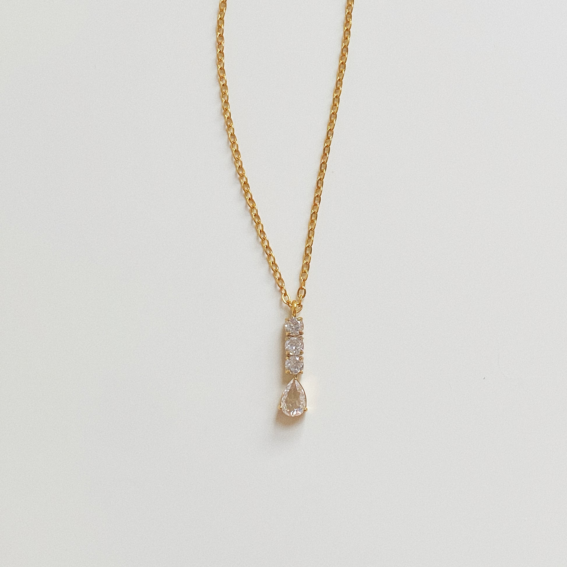 Gold waterproof necklace featuring a vertical bar of three round crystals and a pear-cut teardrop pendant.