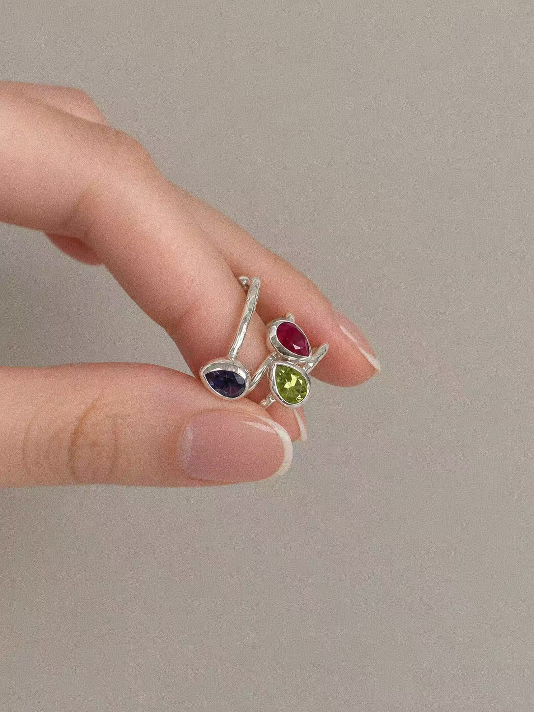 Green peridot teardrop ring held beside two other gemstone rings; jewellery styling image