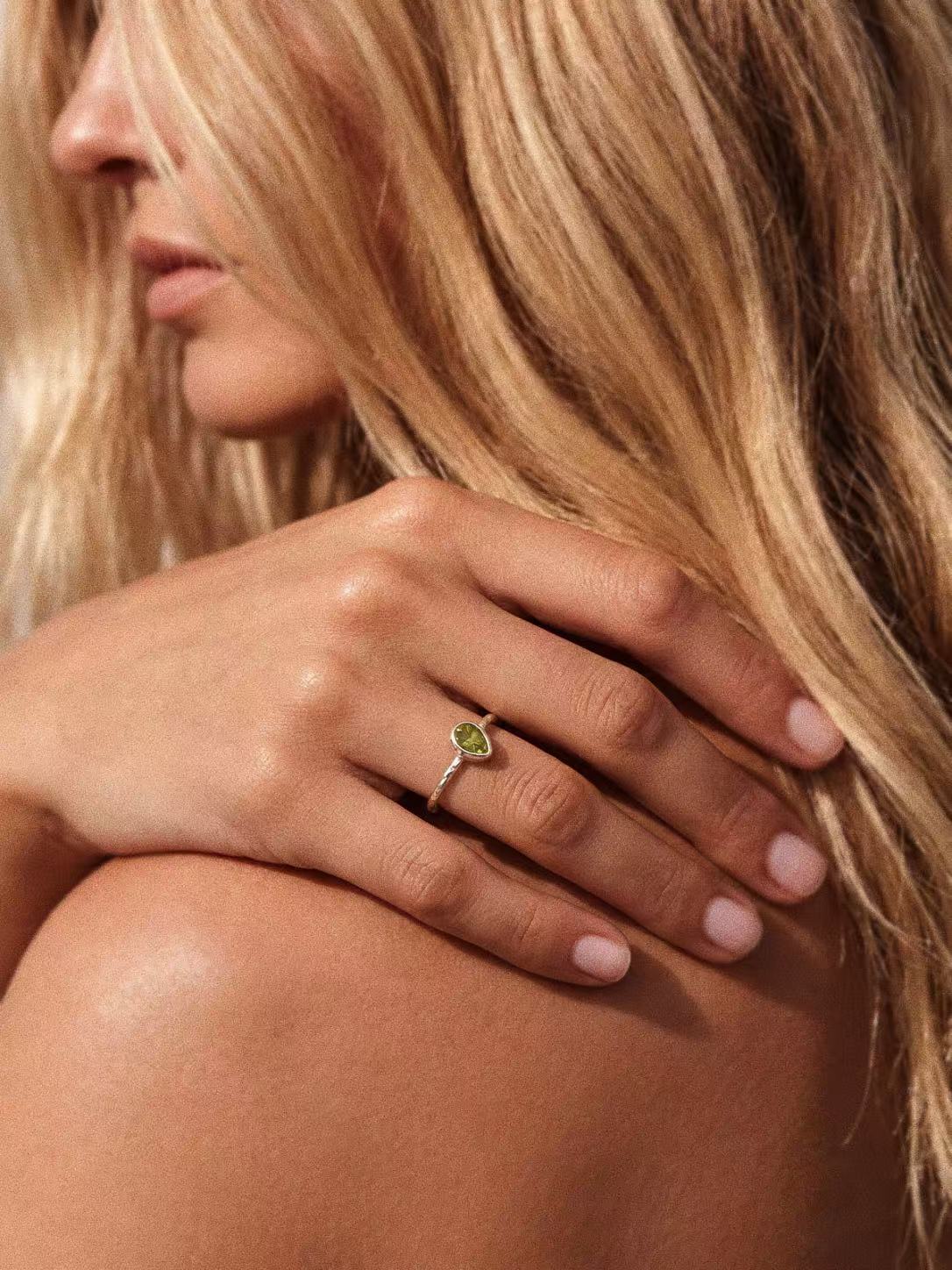 Natural green peridot teardrop ring worn on a hand, showing the silver bezel and slender band