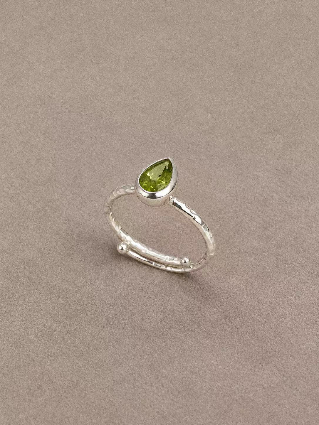 Angled view of the peridot ring showing the pear-shaped green gemstone and sterling silver bezel