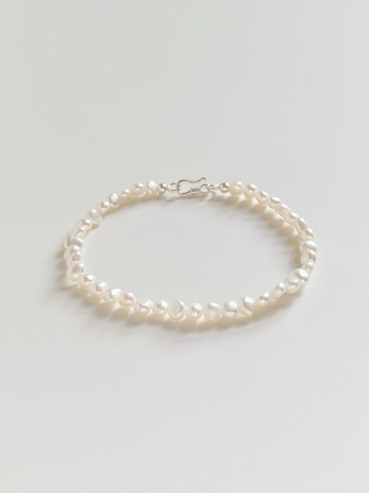Flat lay of a dainty freshwater pearl bracelet featuring 4-5mm baroque pearls and a silver S-hook clasp.
